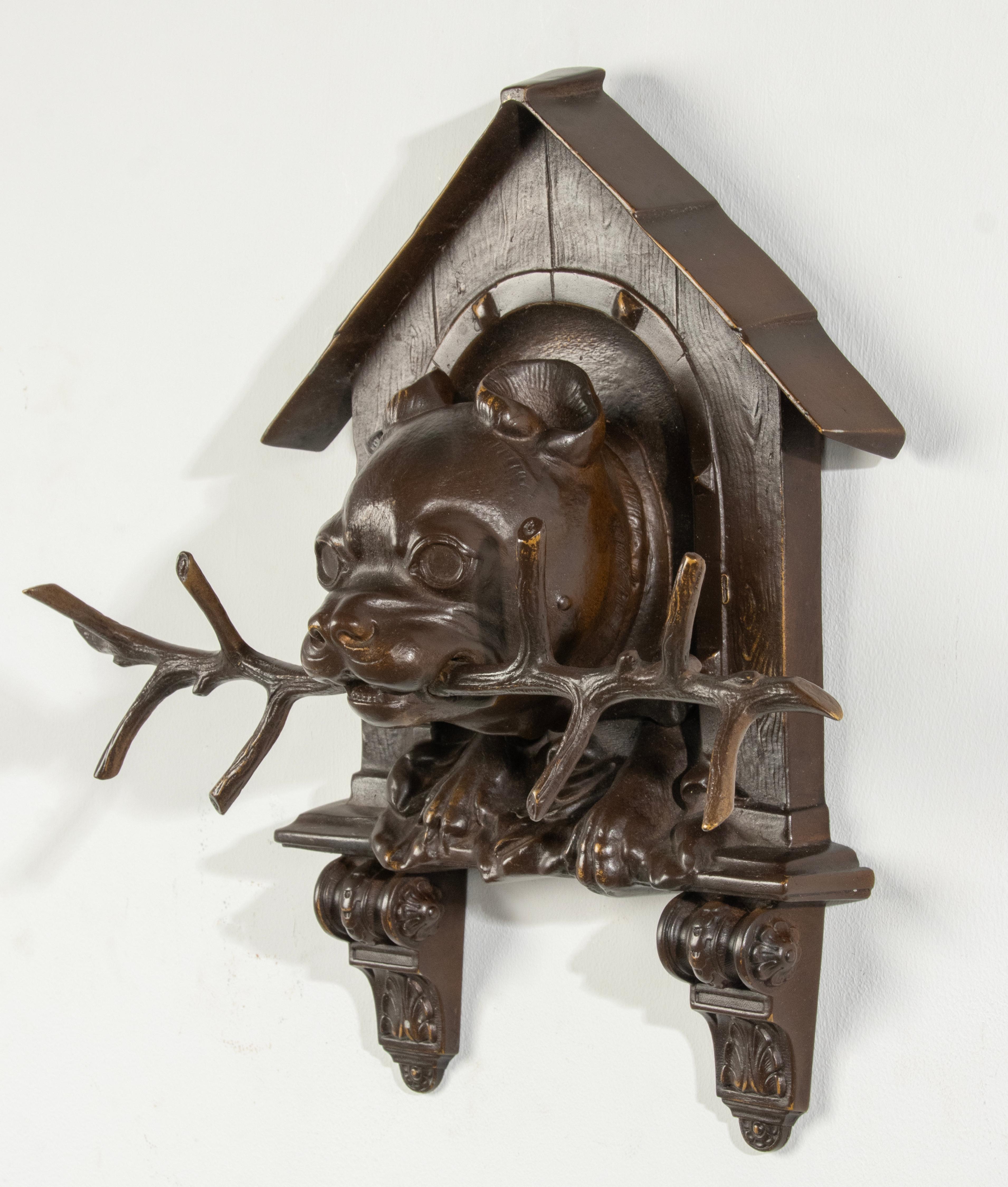 A refined wall sculpture of a Bulldog coming out of a doghouse with a branch in its mouth. Made of brown patinated bronze. With refined casting details such as the wood grain of the wooden doghouse. Made in Germany in Black Forest style, circa