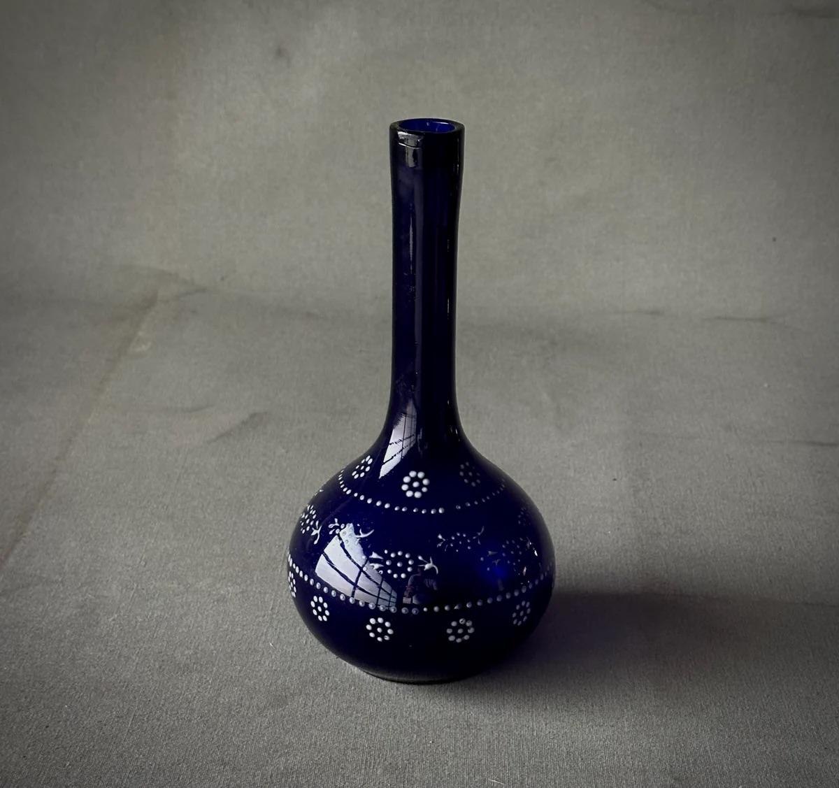 Questa squisita bottiglia da barbiere americana della fine del XIX secolo, realizzata in vetro soffiato cobalto, presenta una ricca tonalità di blu intenso completata da un motivo floreale in smalto bianco dipinto a mano. Il flacone cattura la luce,