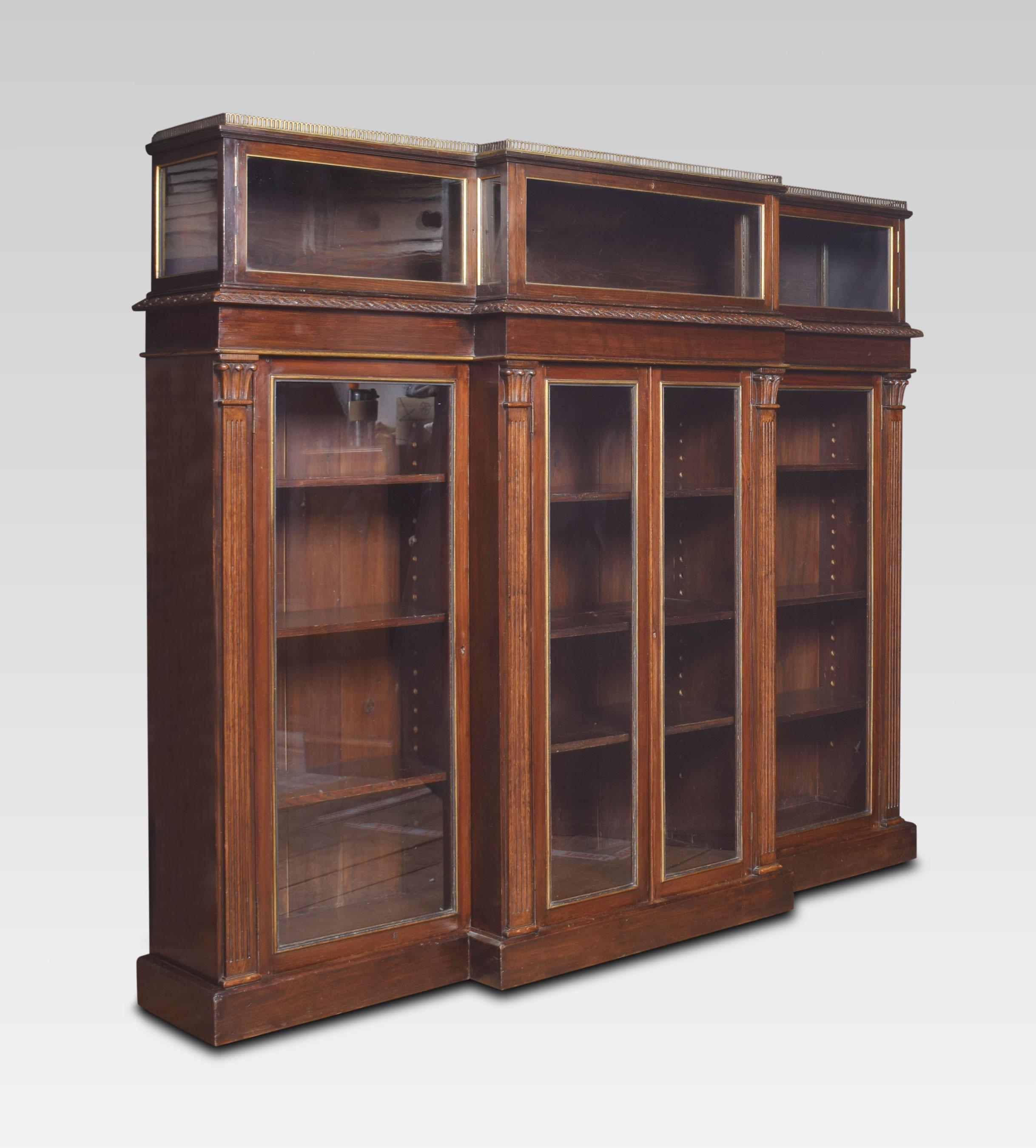 Late 19th century breakfront display bookcase. The raised brass three quarter pierced brass gallery to the unusual display case having a central drop-down door flanked by to cabinet doors. To the large rectangular top with leaf carved mouldings