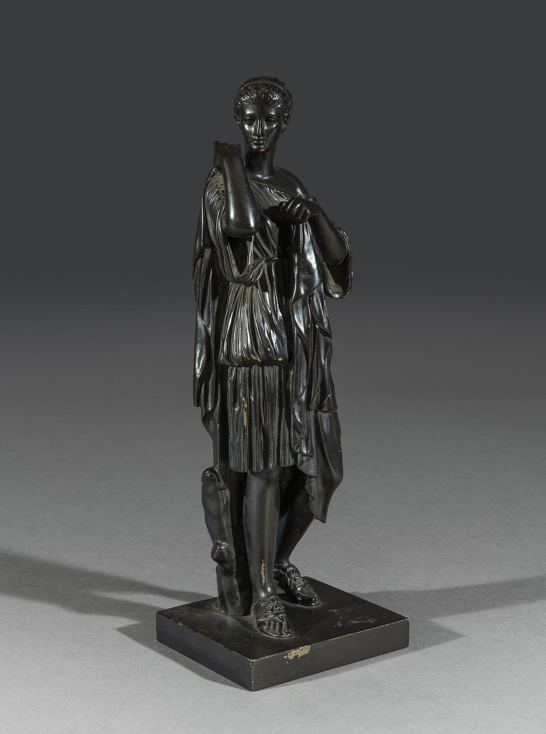 Bronze figure of ‘Diane de Gabies’ cast after the antique marble in the Louvre. The figure, standing by a tree stump, dressed in a chiton bound by two belts, pinning her cloak with her right hand. Original dark patination. Catalogued as ‘Diane De