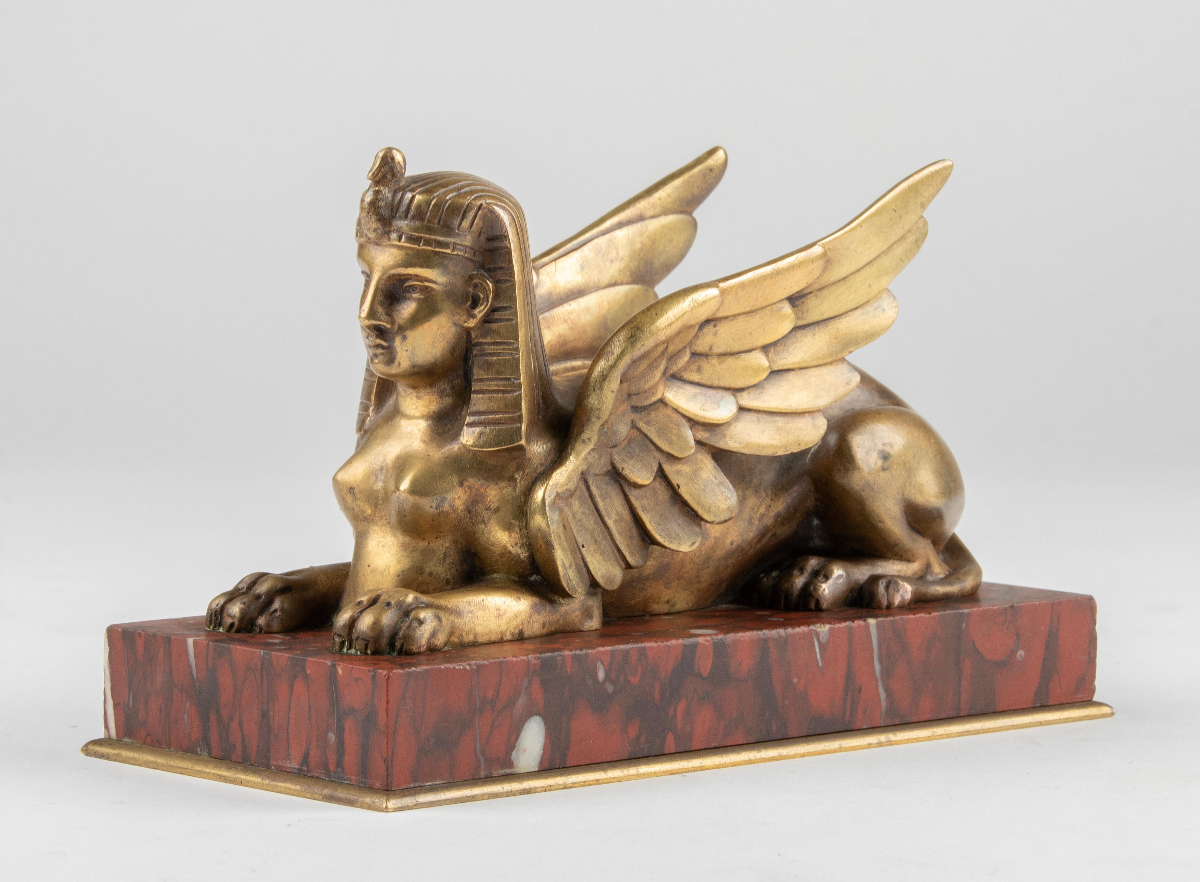 An antique small bronze sculpture of a winged Sphinx, on a red 