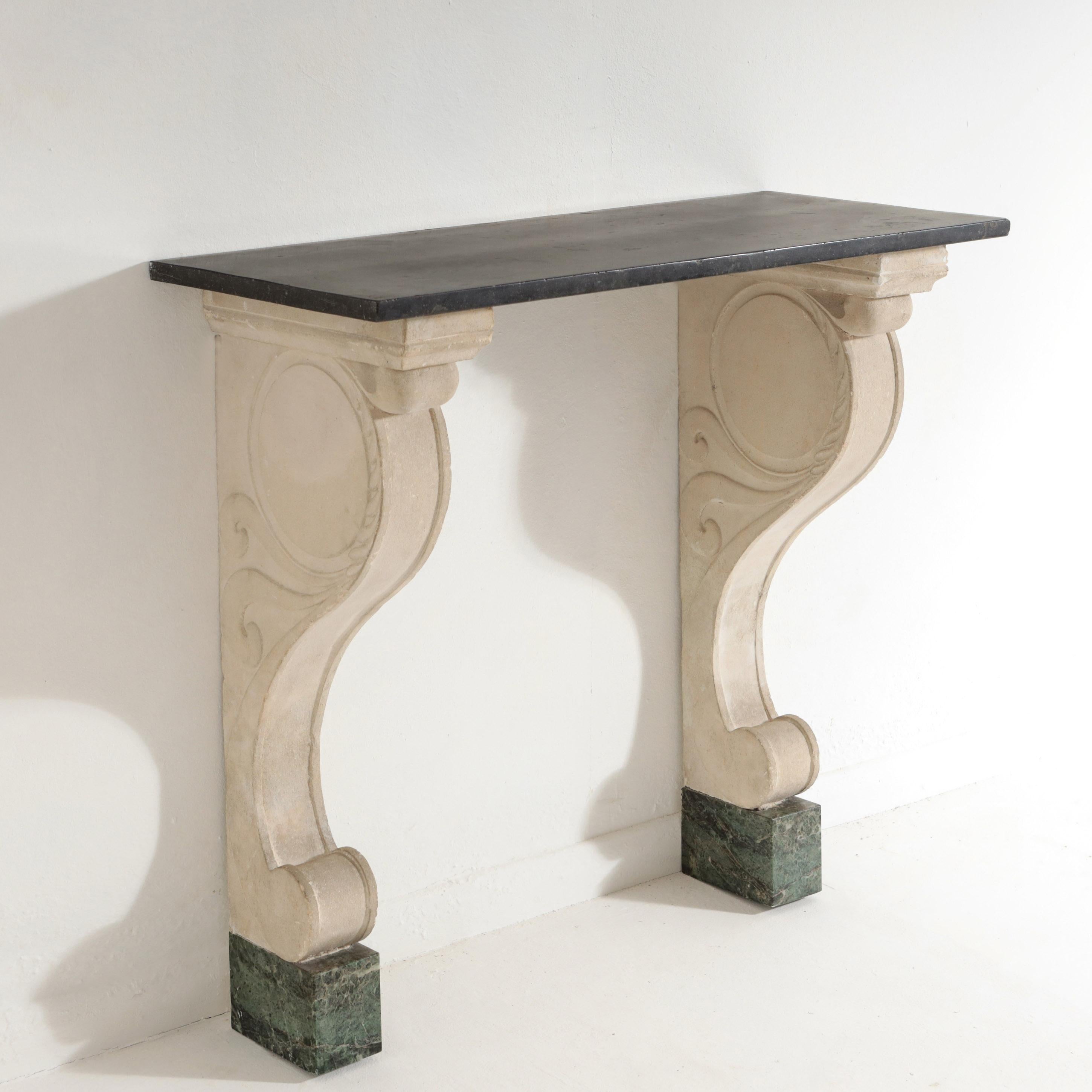 Impressive Carved Stone (Pierre de Bourgogne) and Marble Console Table. Standing on Marble Vert feet, each simple support decorated in elegant, understated, carved relief. Stepped to a black marble top. Both Supports have visible wall fixings at the