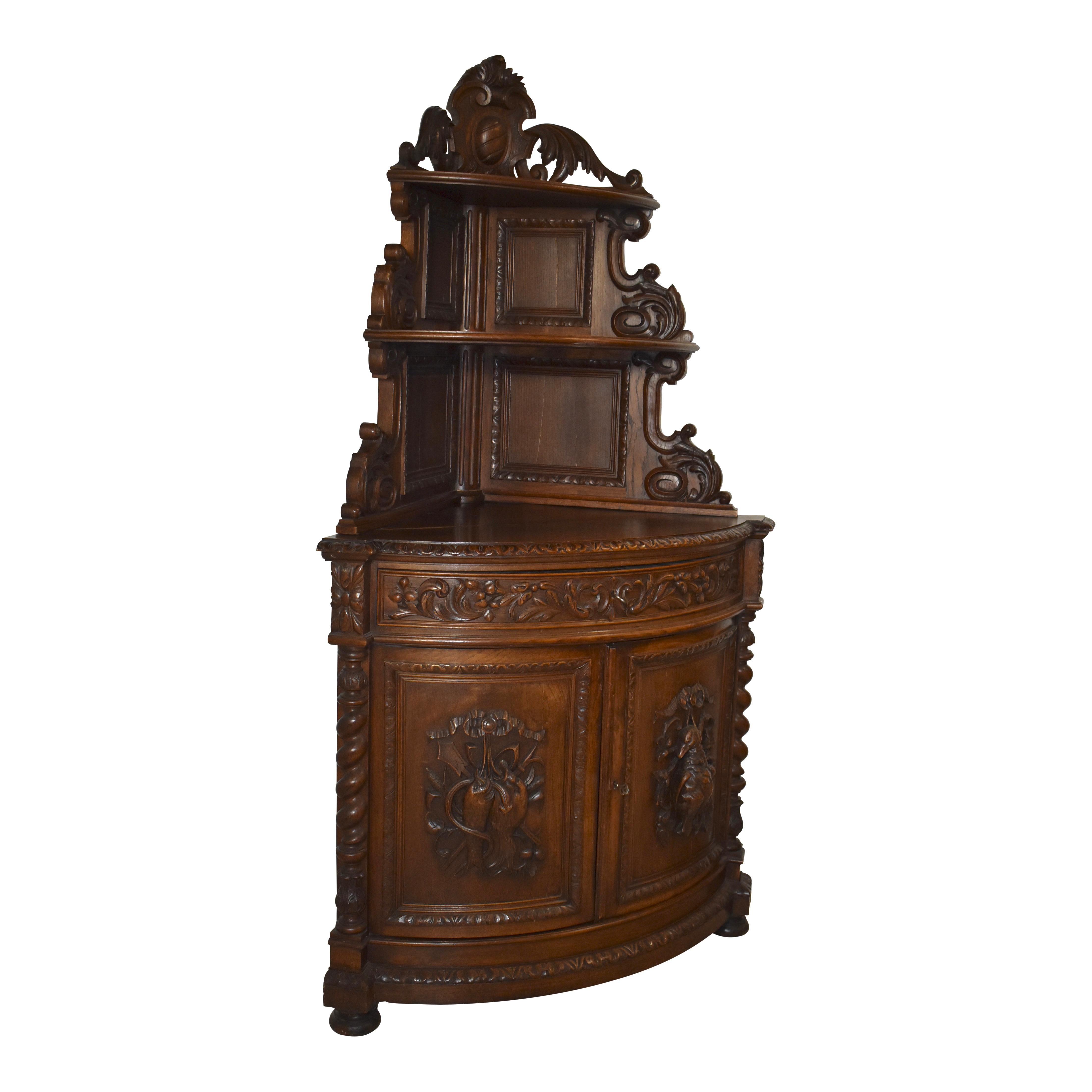Magnificently carved in the late-19th century from solid oak and finished with a rich, dark stain, this handsome corner cabinet showcases bow front construction in both its open shelving at the top and cabinet at the bottom. The open shelving