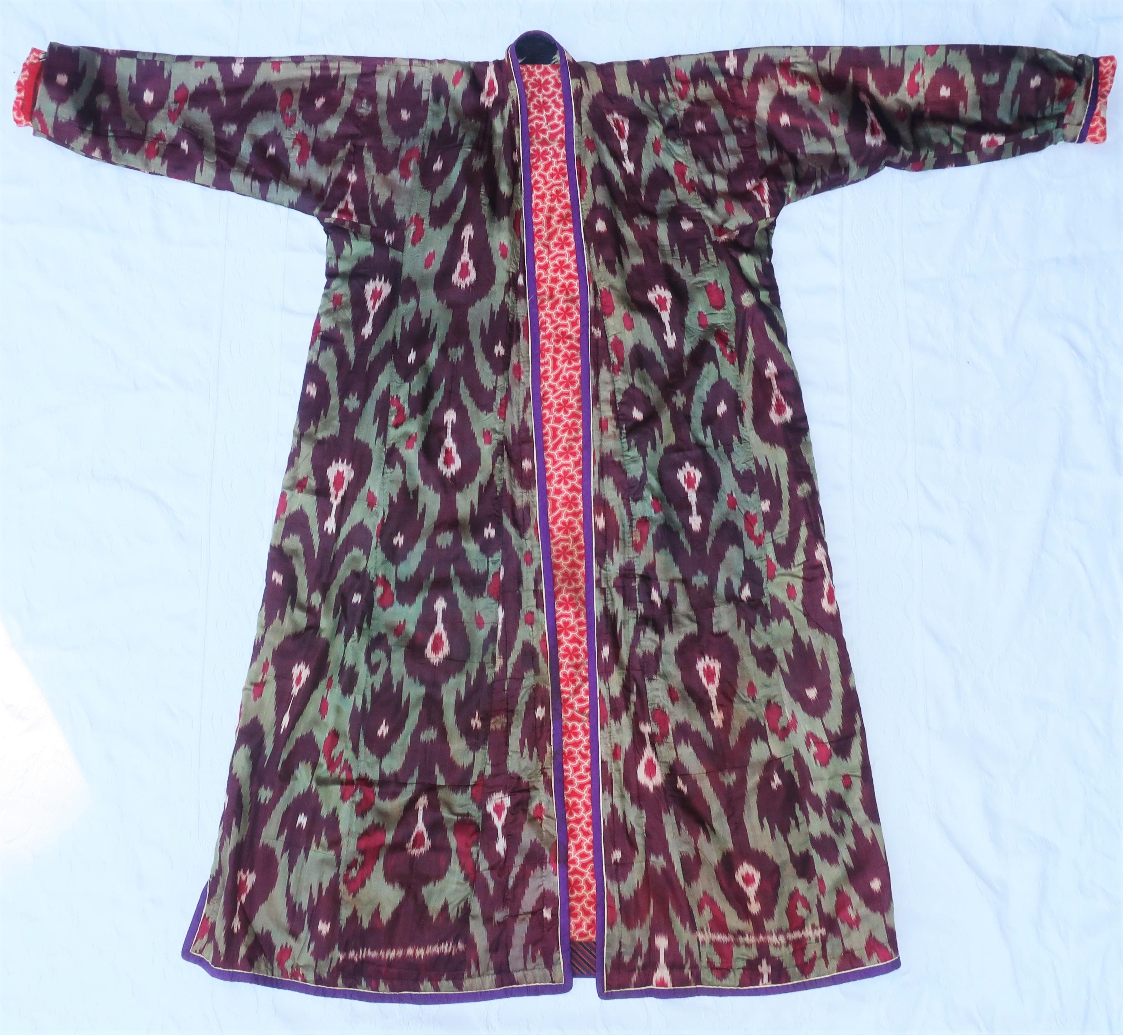 A beautiful late 19th Century silk robe from Central Asia (likely Uzbekistan region) in a traditional Ikat pattern displaying shades of purple, aubergine, red and green.  It is lined in a red and white cotton floral with banding in blue, red and