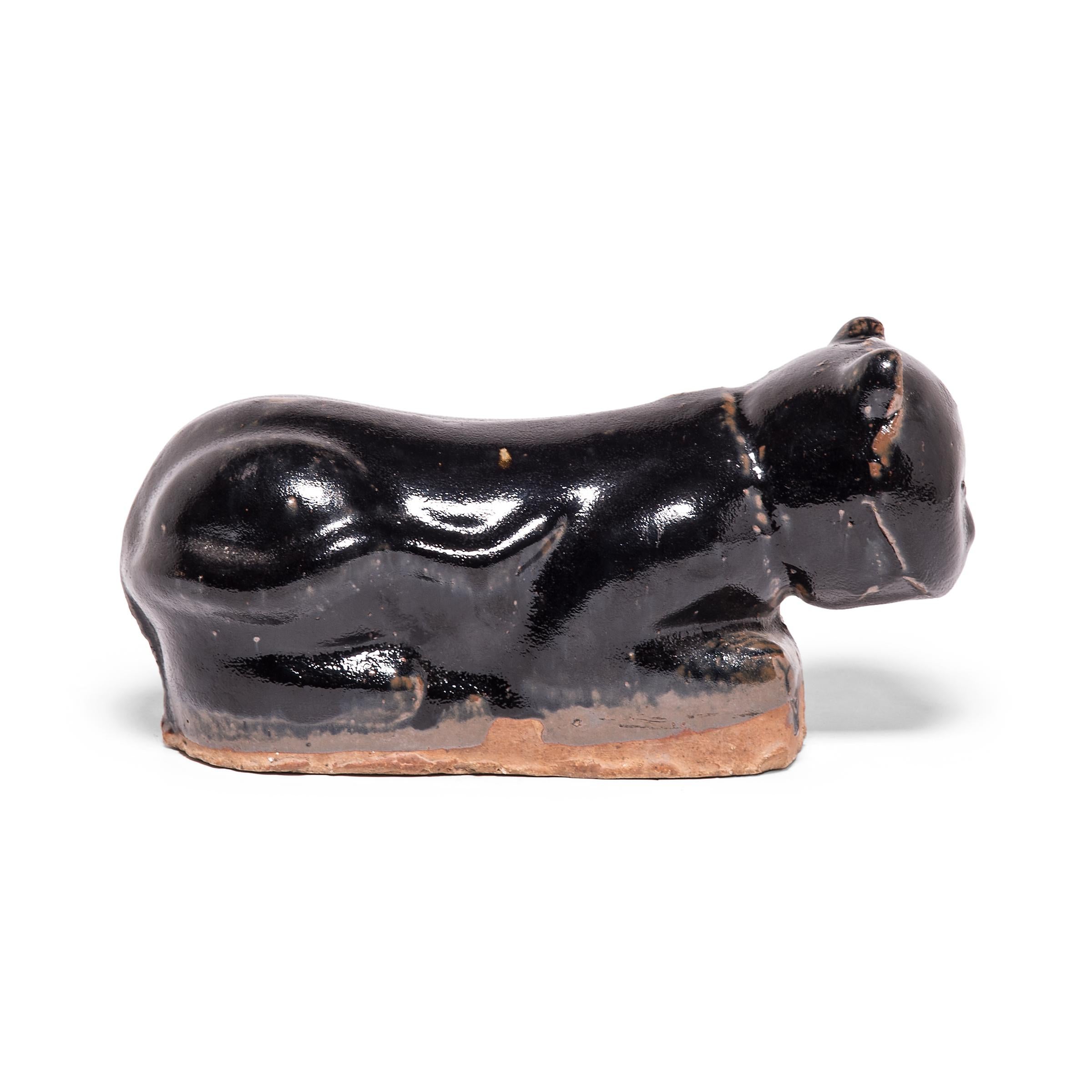 To keep her elaborate hairstyle intact while sleeping, a well-to-do Qing-dynasty woman once used this ceramic headrest as a pillow. The headrest is shaped as a crouching house cat, cloaked in a beautifully irregular pitch black glaze. Drawn upon its