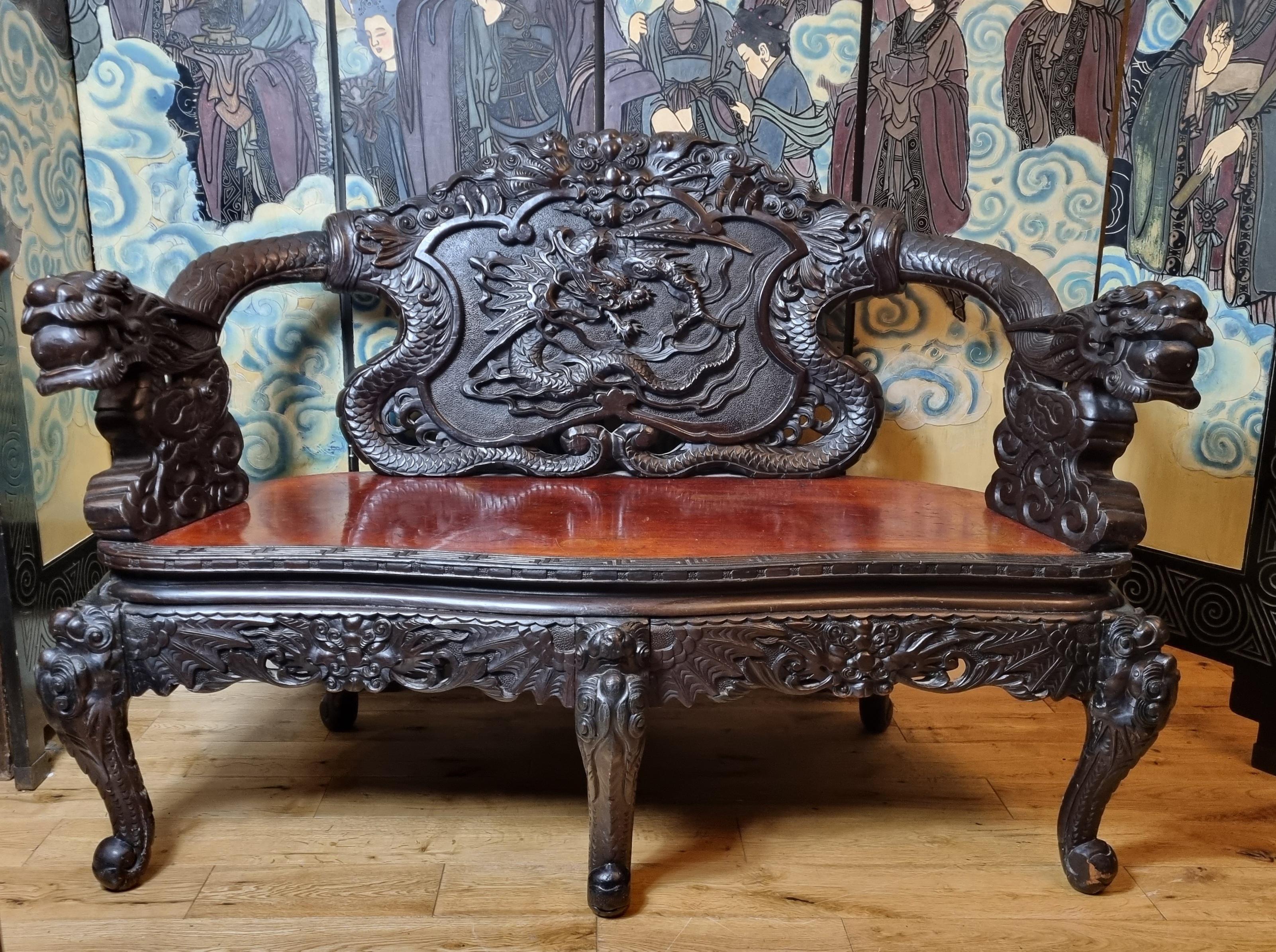 Eine beeindruckende chinesische Bank aus dem späten 19. Jahrhundert, kunstvoll aus Hartholz geschnitzt und mit aufwendigen Drachenmotiven verziert. Die Handwerkskunst zeigt außergewöhnliche Liebe zum Detail, mit zwei kühnen, wilden Drachenköpfen,
