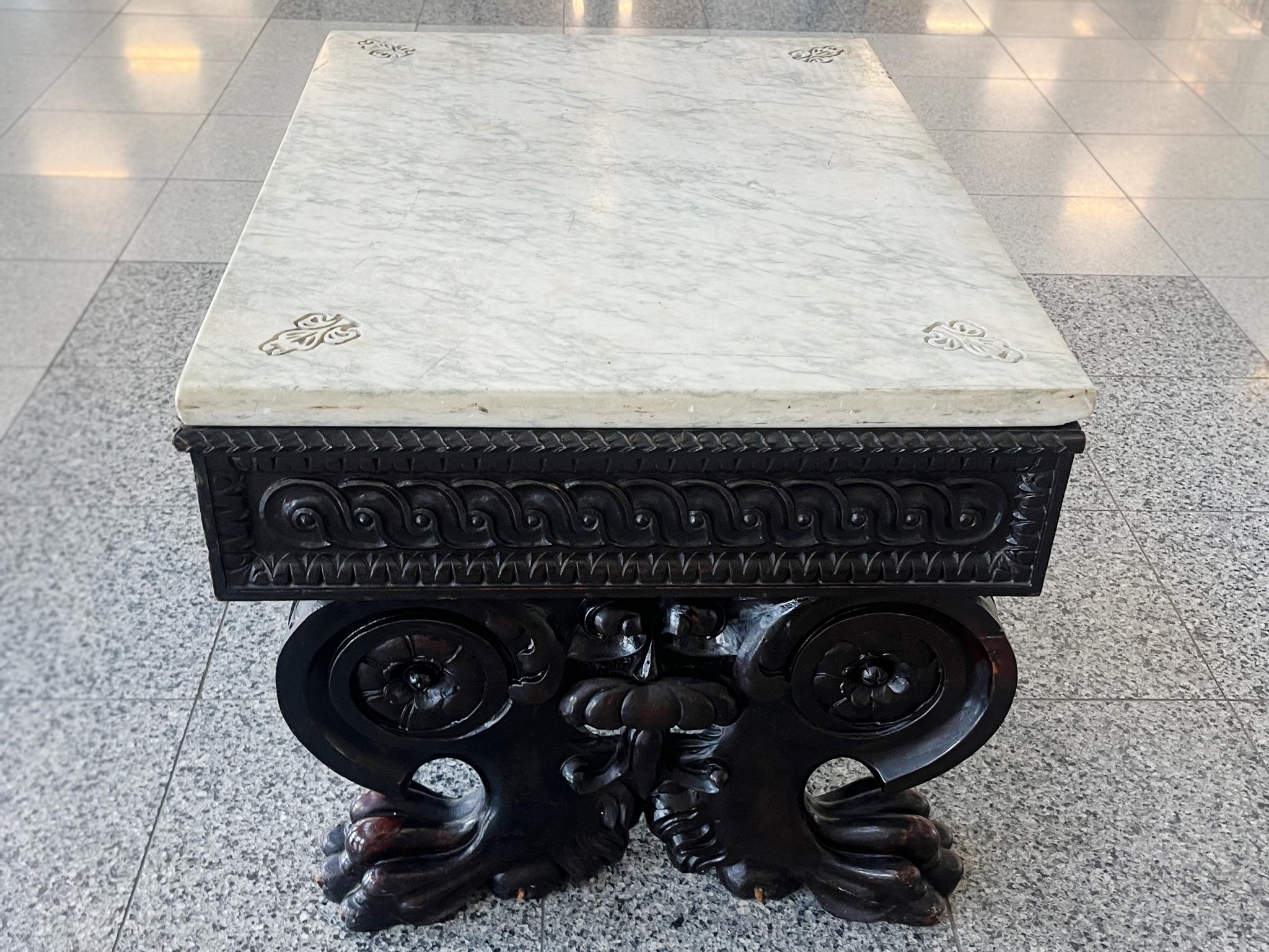 Fabricada a mano a finales del siglo XIX, esta mesa baja china consta de una base de madera y un tablero de mármol blanco. La base destaca por su talla muy ornamentada, con detalles florales y en volutas que culminan en pies de garra. La superficie