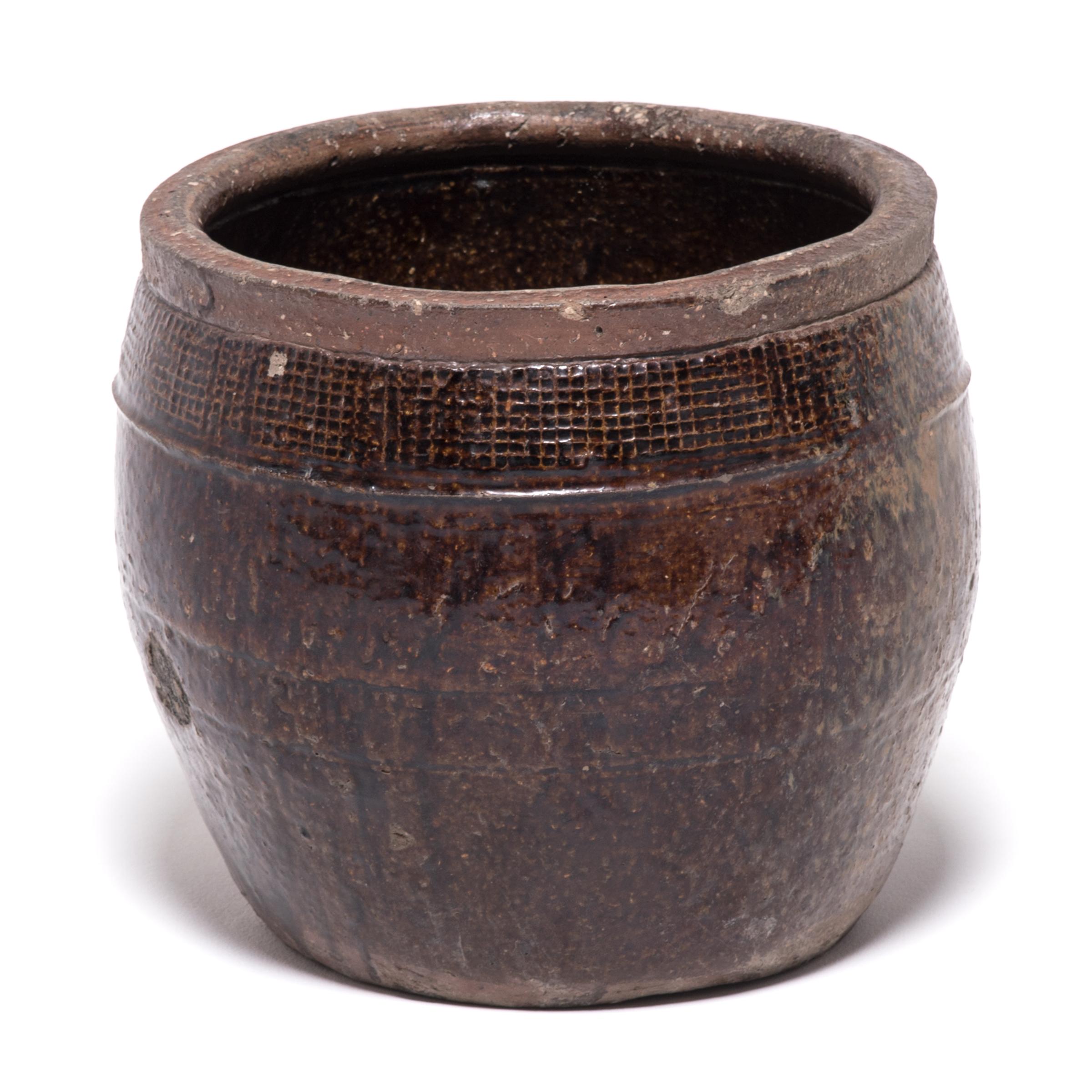 The potter who crafted this large, wide-mouthed jar in Beijing used contrasting textures to add interest to the vessel’s simple barrel shape. Small grids incised just under the unglazed rim draw the eye to the upper portion, while the free