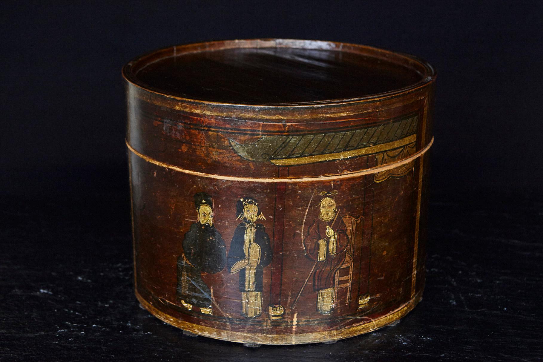 Very decorative late 19th century Chinese hand-painted and gilded round wooden hat box.
The (probably) elm wood box has been treated with a dark stain, then decorated with a hand painted scene with people and gilded edges. Fantastic piece with a