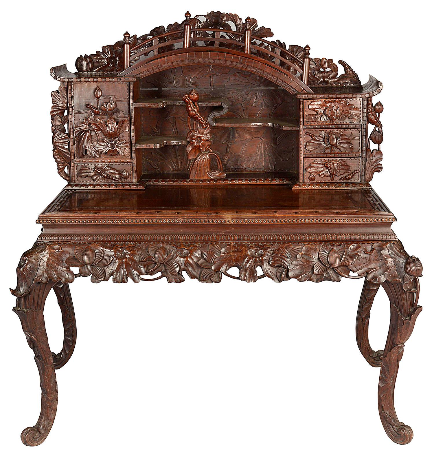 A very impressive fine quality Japanese hardwood desk from the Meiji era, having a bridge like structure to the top, shelves, cupboards and drawers all with wonderful carved floral and leaf decoration, as is the frieze and raised on elegant cabriole