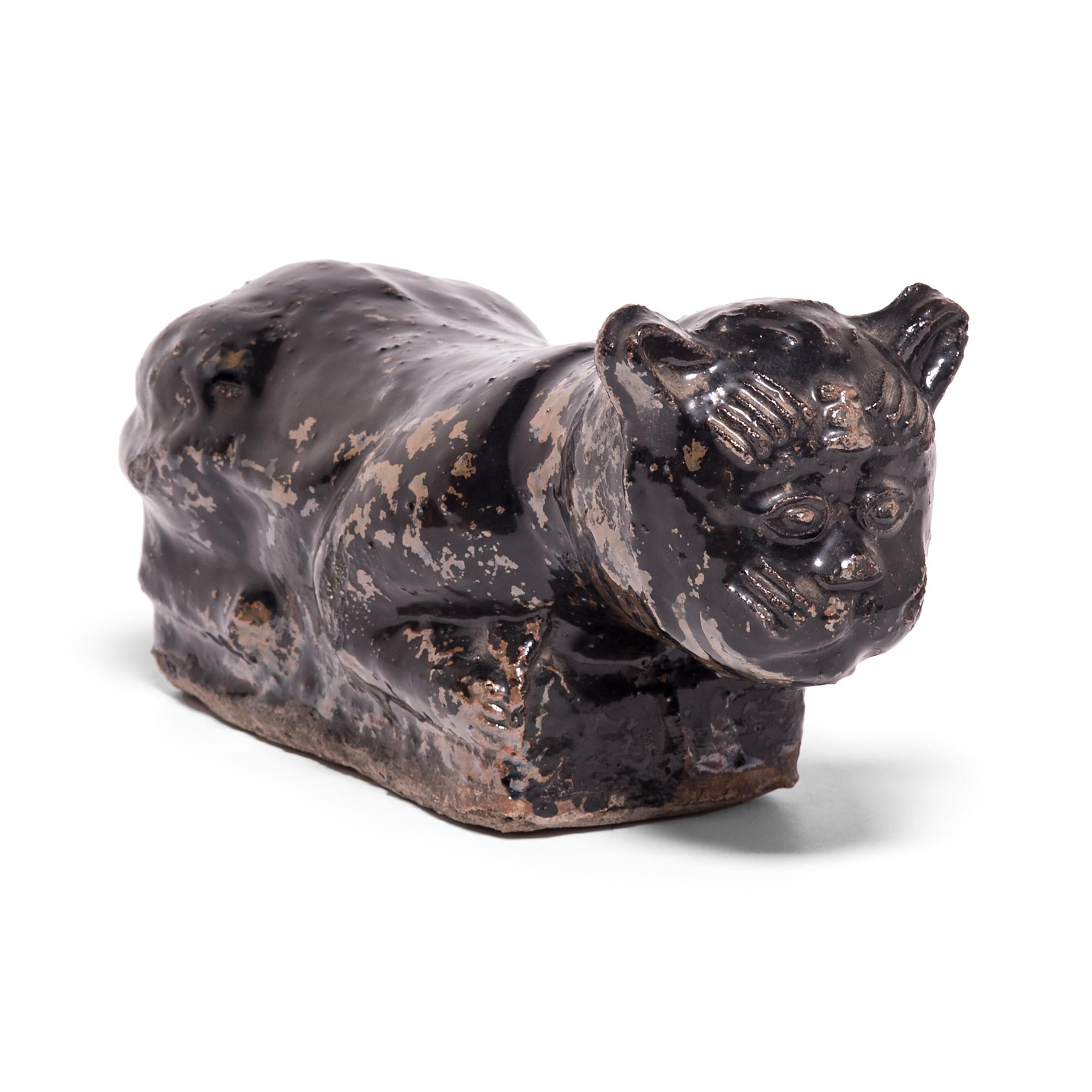 To keep her elaborate hairstyle intact while sleeping, a well-to-do Qing-dynasty woman once used this ceramic headrest as a pillow. The headrest is shaped as a crouching house cat, cloaked in a beautifully irregular dark brown glaze. Drawn upon its