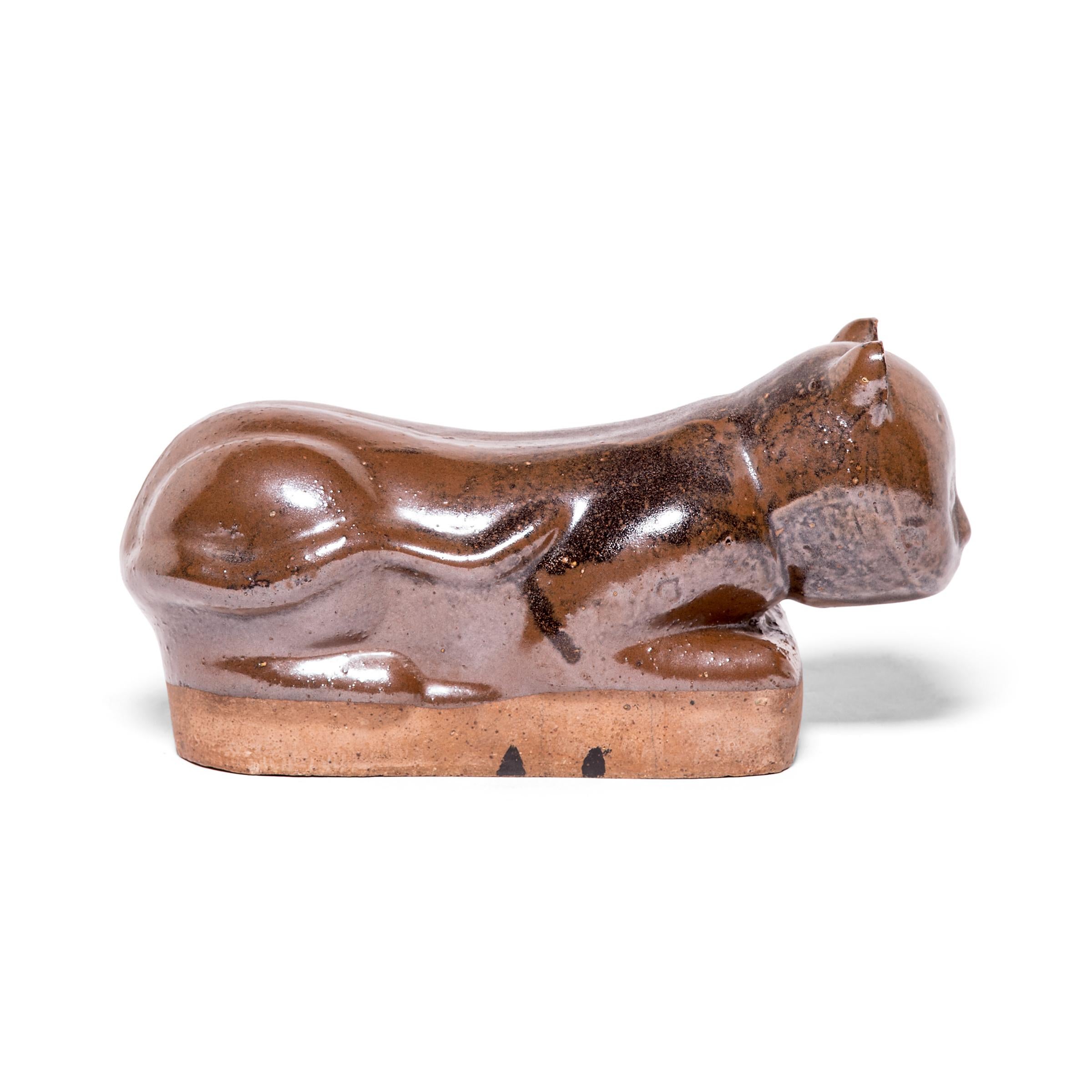 To keep her elaborate hairstyle intact while sleeping, a well-to-do Qing-dynasty woman once used this ceramic headrest as a pillow. The headrest is shaped as a crouching house cat, cloaked in a beautifully irregular warm brown glaze. Drawn upon its