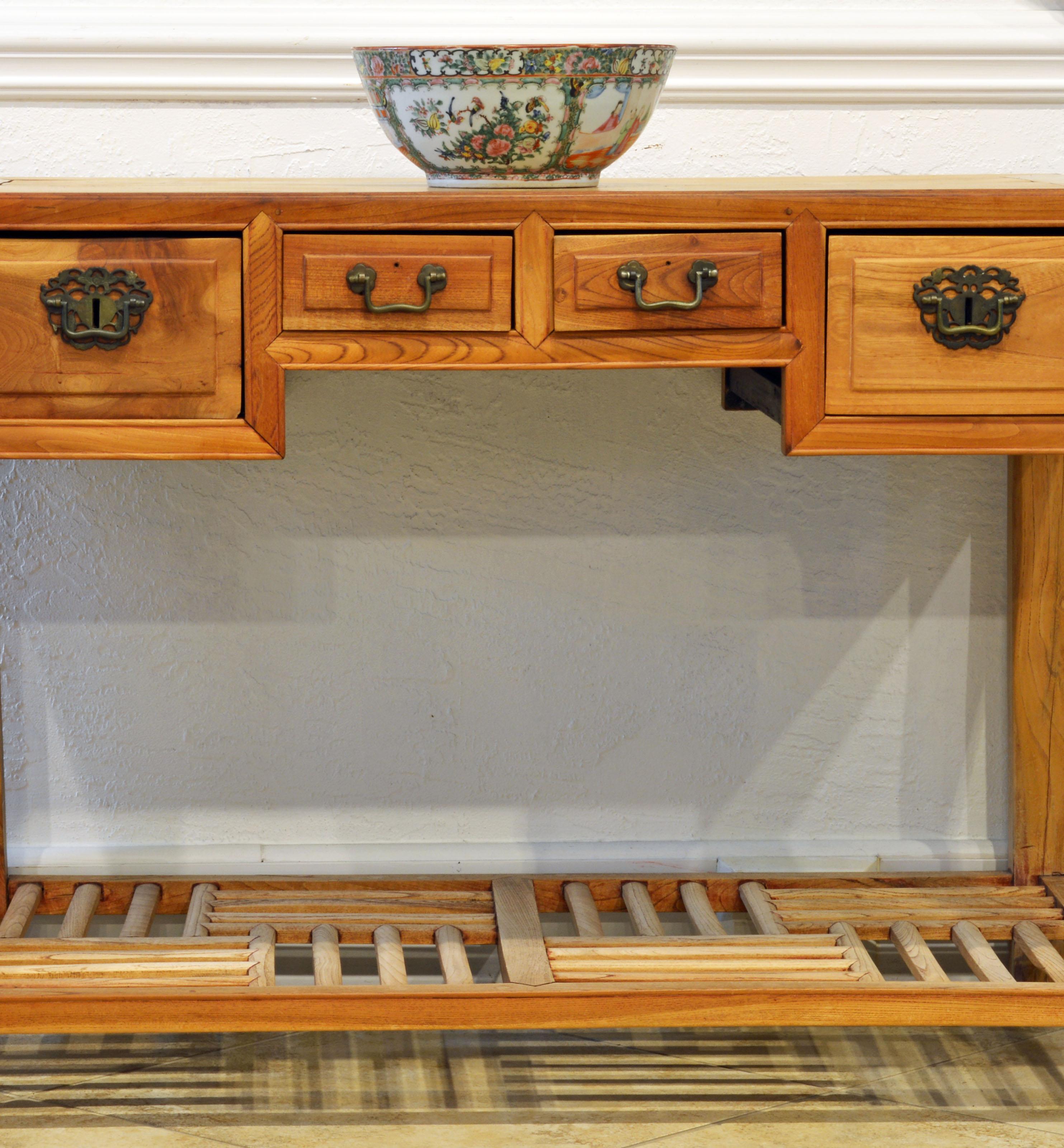 This late 19th century Chinese natural color elm wood desk features two center small drawers flanked by two deeper drawers. The legs are joined by a low lattice shelf in a traditional Chinese pattern.