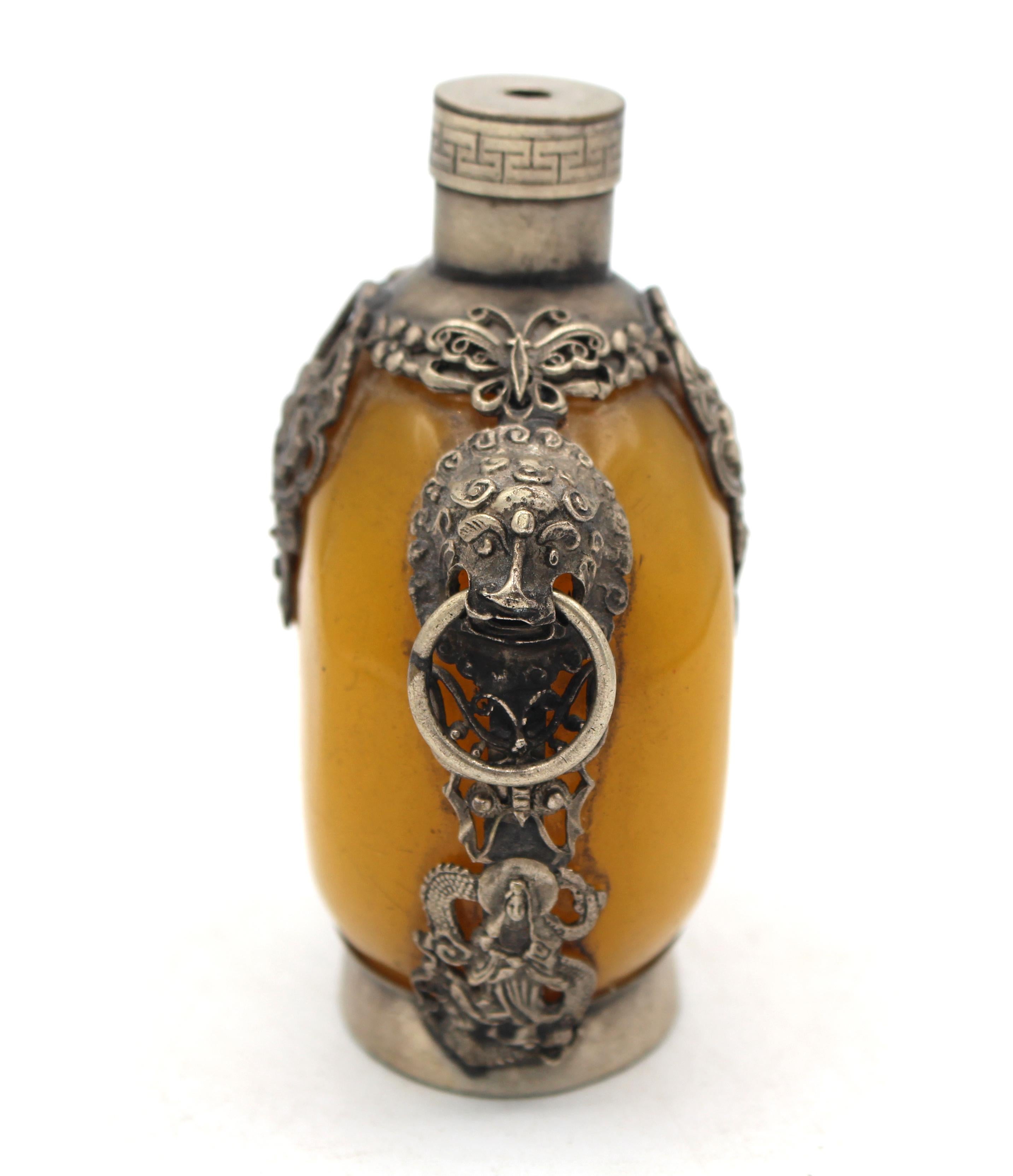 Late 19th century Chinese or Tibetan snuff bottle. Silver colored elaborate mounts surround the beeswax round bottle. Lion mask ring handles, flower baskets & goddesses on the sides. Lacks stopper. Signed. 3.25