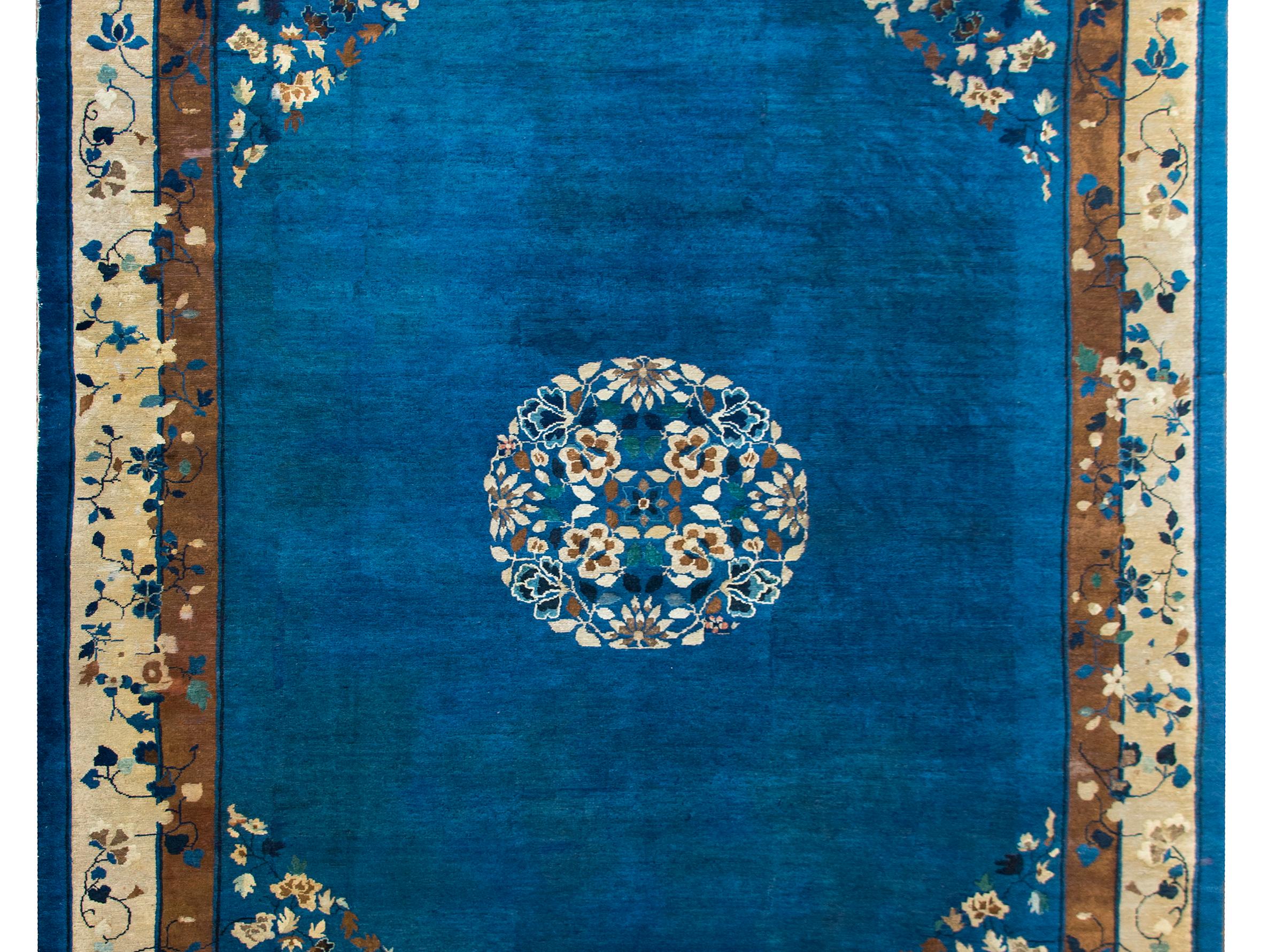 A wonderful late 19th century Chinese Peking rug with a round peony, chrysanthemum, and cherry blossom medallion set against an indigo background, and surrounded by a complex border with brown, cream, and indigo stripes overlaid with more scrolling