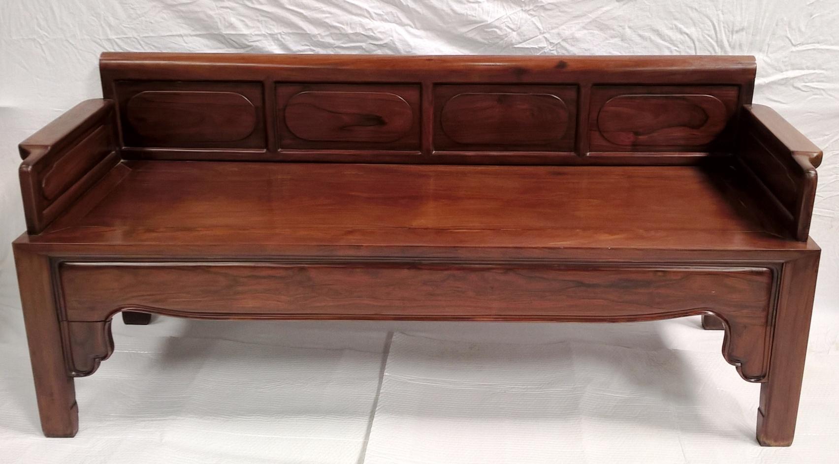 A good sized late 19th century Chinese rosewood bench seat.

The raised back with four panels, each with a shallow carved lozenge to the centre and arm rests to each side.

The whole raised on four square legs united by a shaped frieze to the