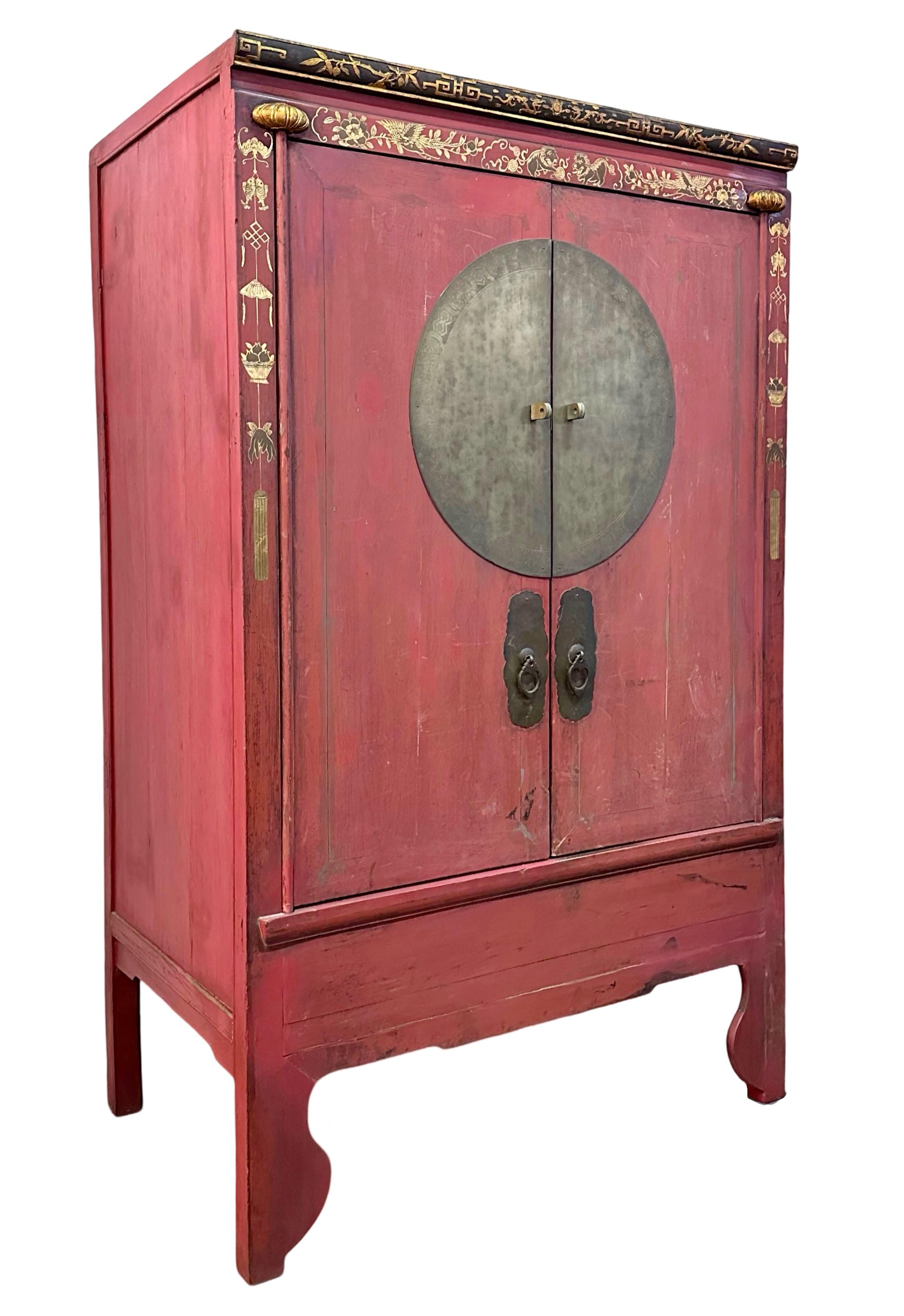An antique wedding cabinet from Zhejiang province, with beautiful original red lacquer, and original round brass plate and door pulls. This round brass plate is especially large and measures 51.5cm in diameter. It has shallow engravings around the