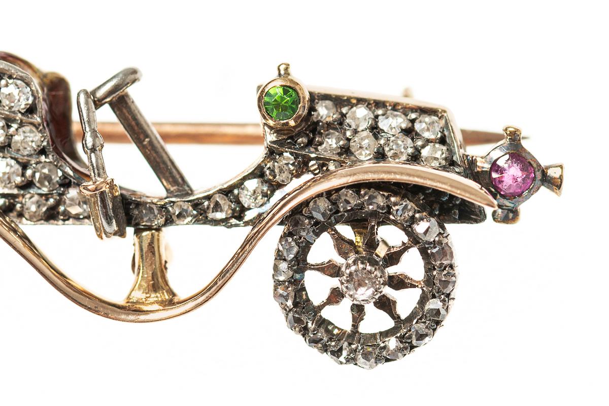 A late 19th century brooch of a vintage motor car in particularly fine detail. The body is set with brilliant cut diamonds, the horn set with a green garnet and the headlight set with a Burma ruby. The revolving wheels are set with a central