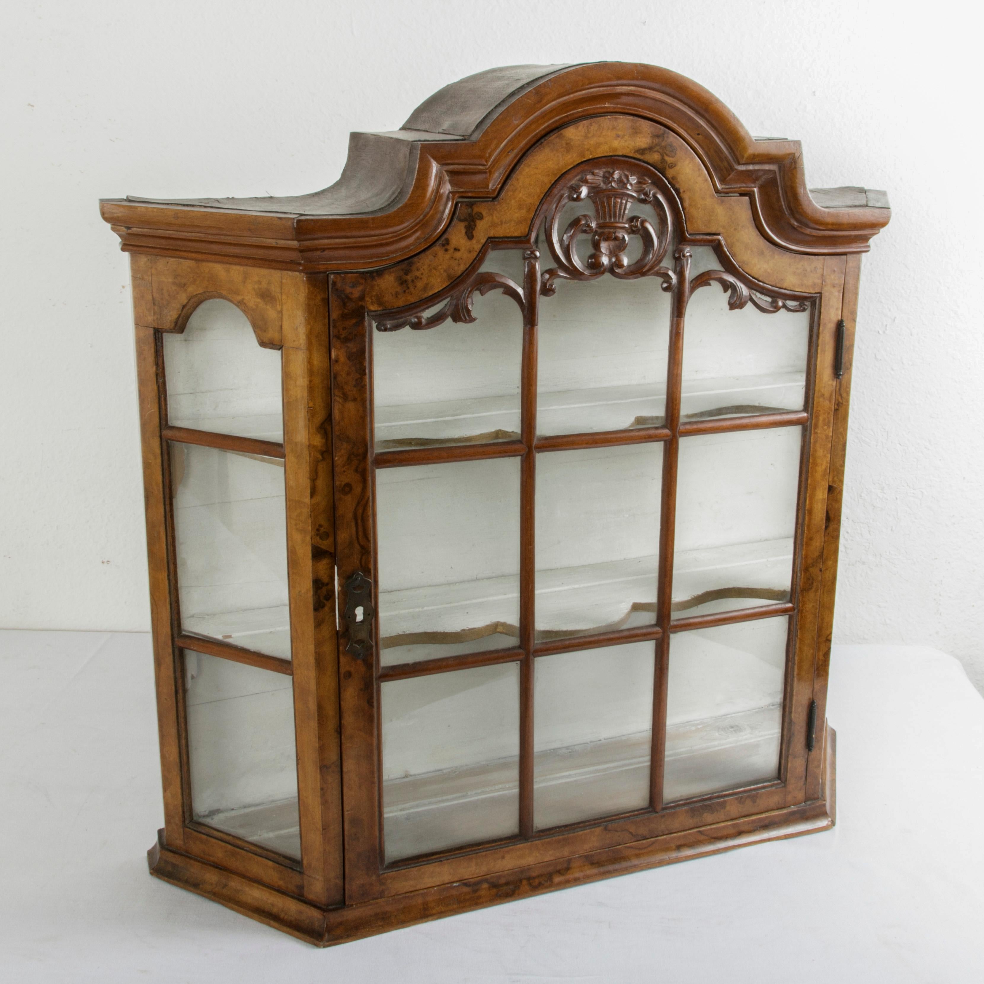 This Dutch wall vitrine or tabletop display cabinet from the late 19th century features a solid walnut case and its original glass panes on three sides set into mullions. The top of the door at the front is detailed with a central hand carved