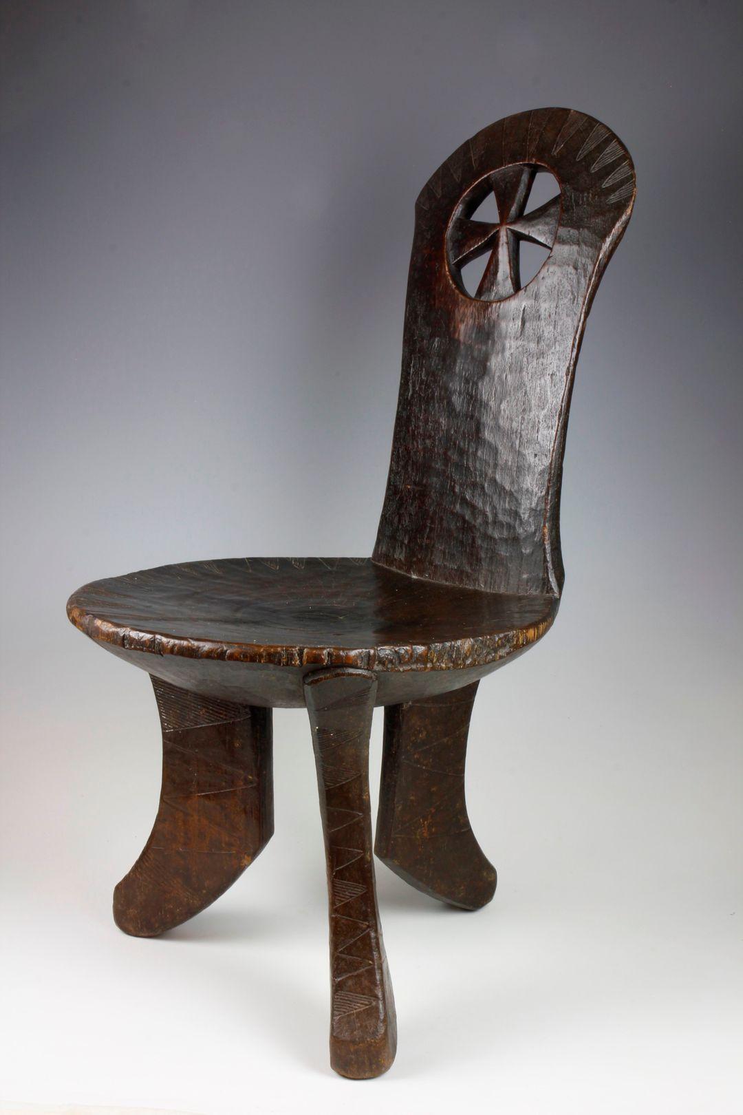This finely carved, medium-sized chair from the Jinka culture in Ethiopia features an upright back-support with an unusual and attractive cut-out cross decoration. 

A series of downward pointing triangular designs filled with striations are located