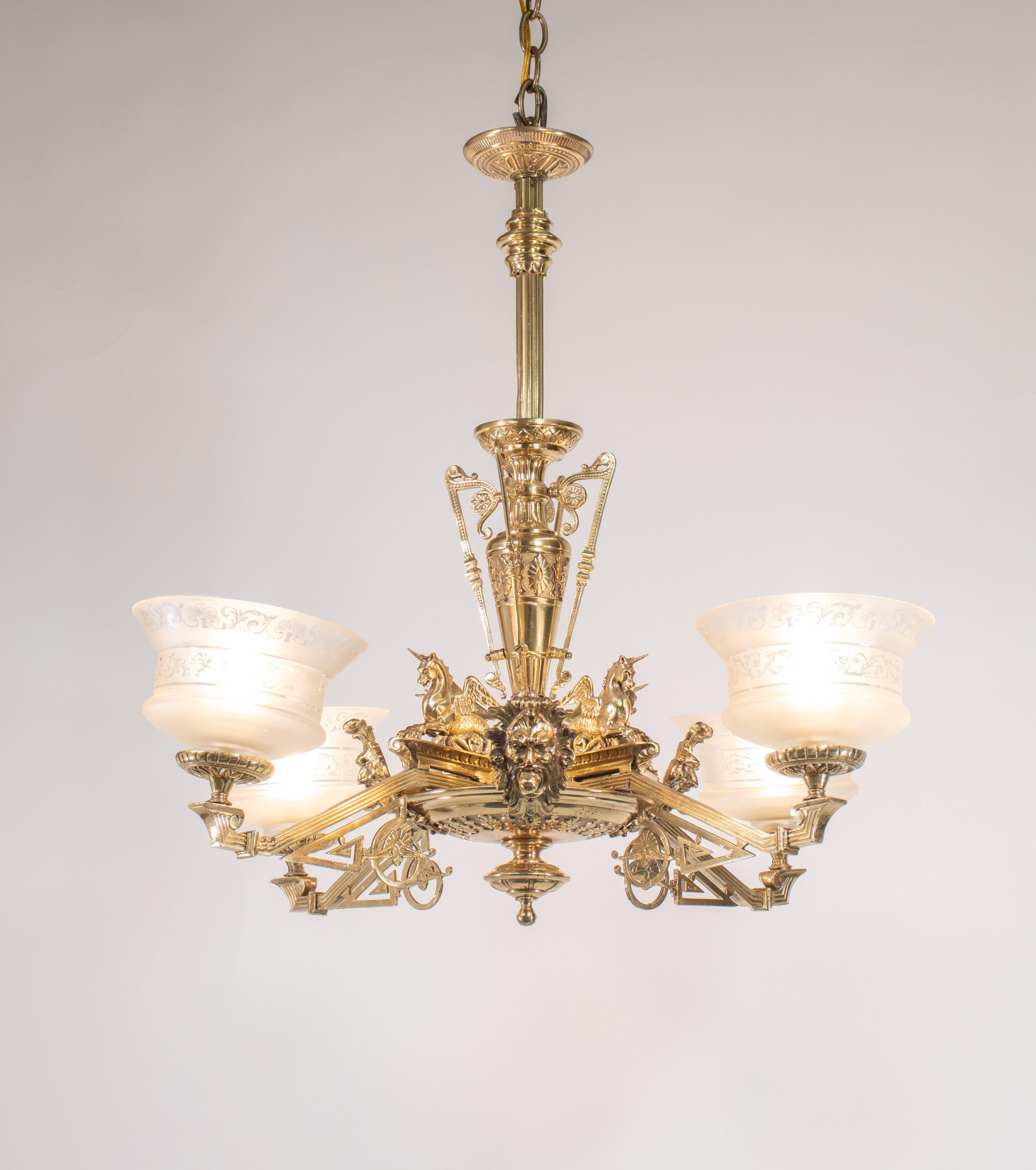 Questo lampadario di fine Ottocento in bronzo dorato e ottone in stile Eastlake ha quattro luci, paralumi in vetro acidato e dettagli a voluta. L'intero lampadario enfatizza l'iconografia e gli stili neoclassici. Il corpo è ornato da cavalli marini