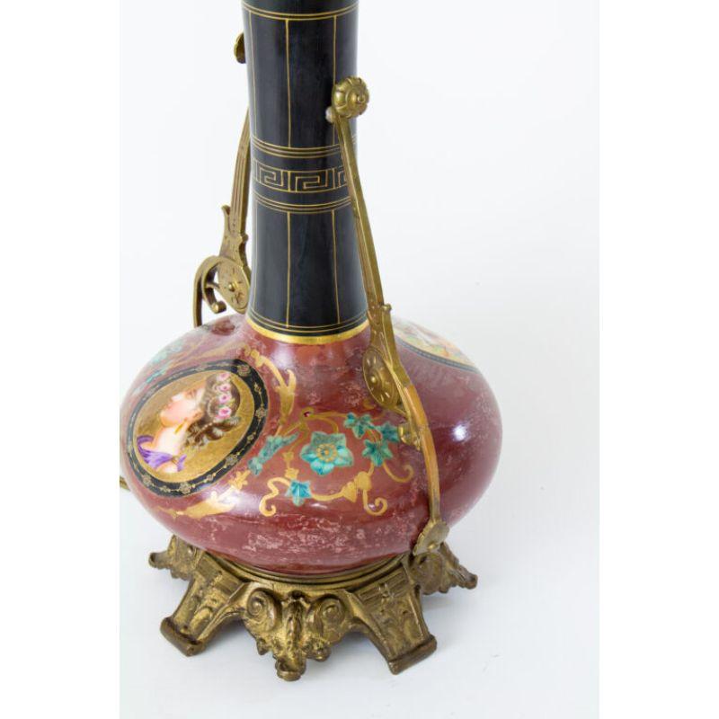 This lamp is porcelain in a dark crimson with a hand painted cameo on one side and instruments on the other. The arms and base are metal. It was originally made to be a gas lamp, but has since been electrified. In very good condition, some wear and