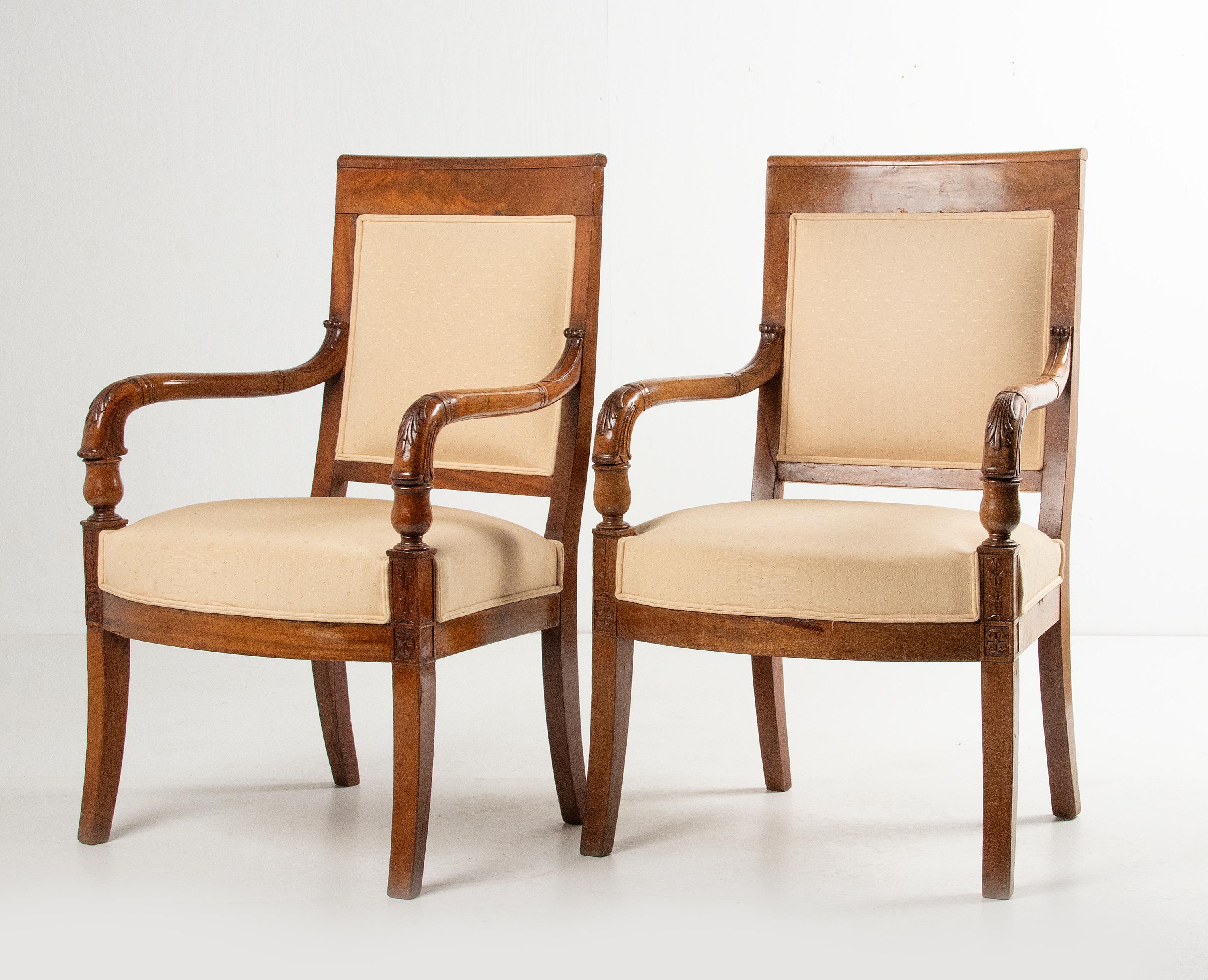 A pair of antique Empire style armchairs. The armrest and legs are made of solid mahogany, the backrest is made of veneered mahogany. An elegant design with curved armrests and tapered Sabres leg. The construction is in good and solid condition, and