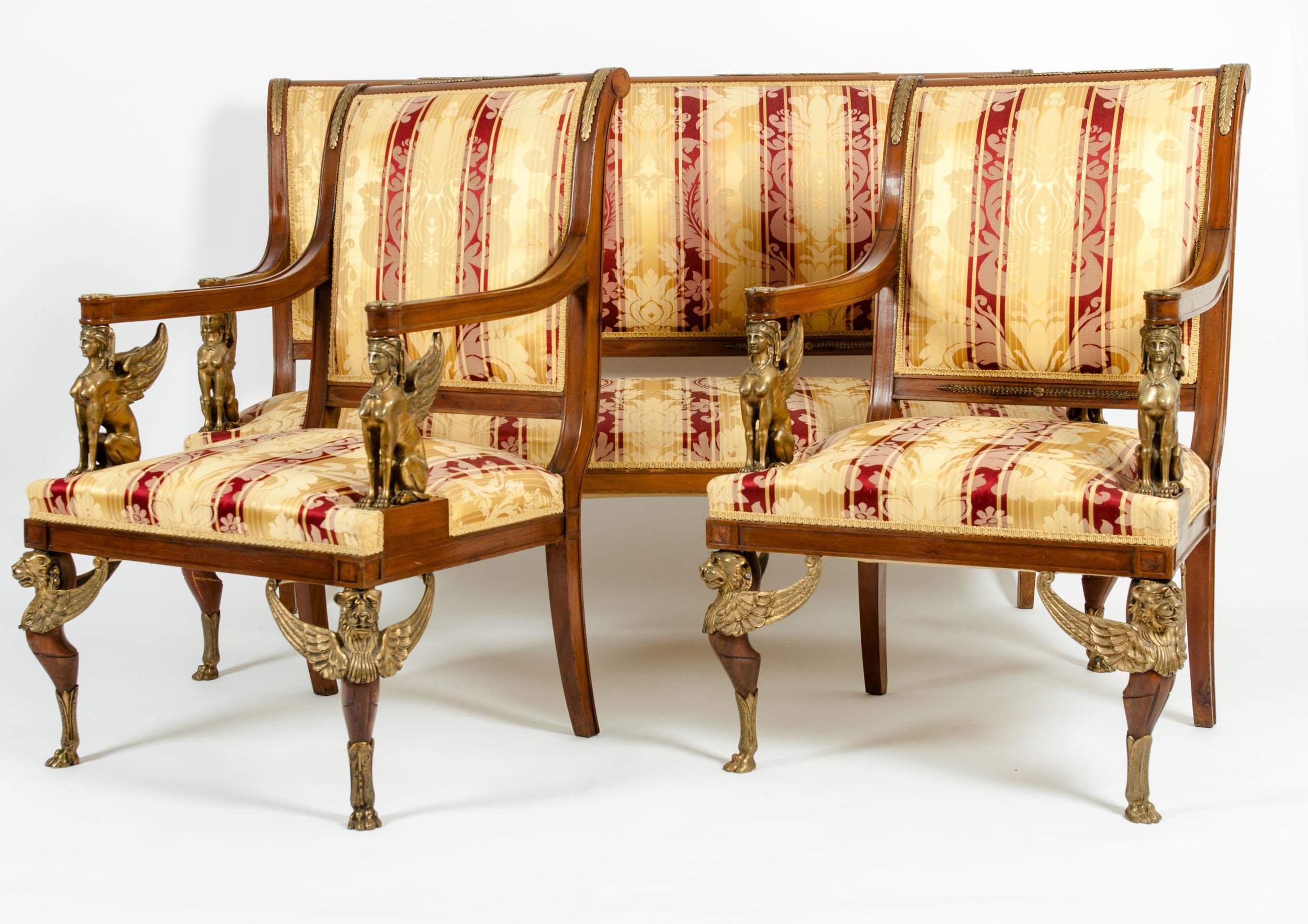 Spectacular late 19th century French Empire style handcrafted three piece gilt bronze salon suite. One upholstered sofa & one pair of armchairs. The armchairs are set on four straight mahogany legs, the front two of which are set on gilt bronze paw