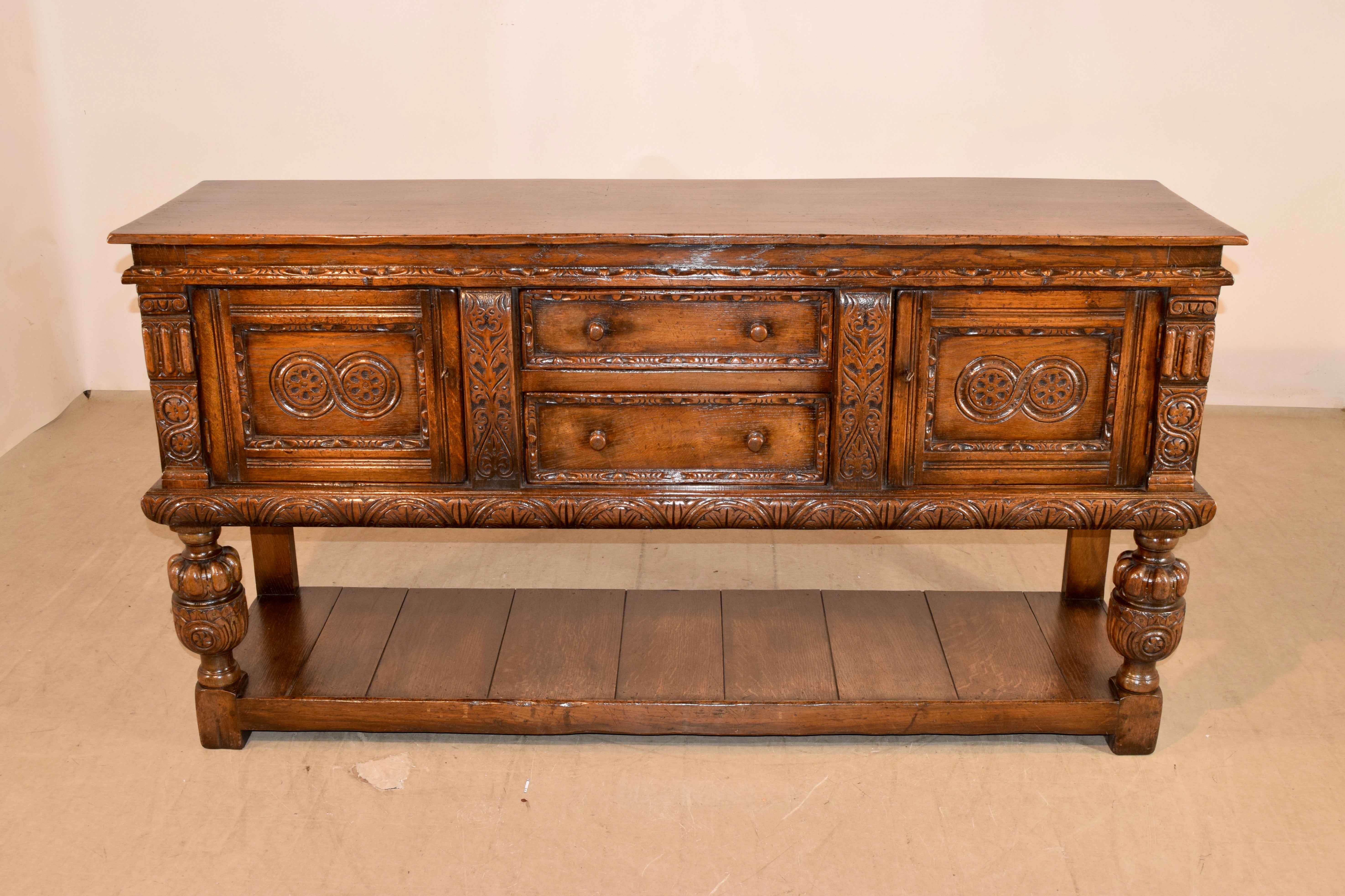 19th century oak pot board from England with a two board top over hand paneled sides and two central drawers in the front, both with lovely hand carved banding on the drawer fronts. The central drawers are flanked by paneled doors which have been