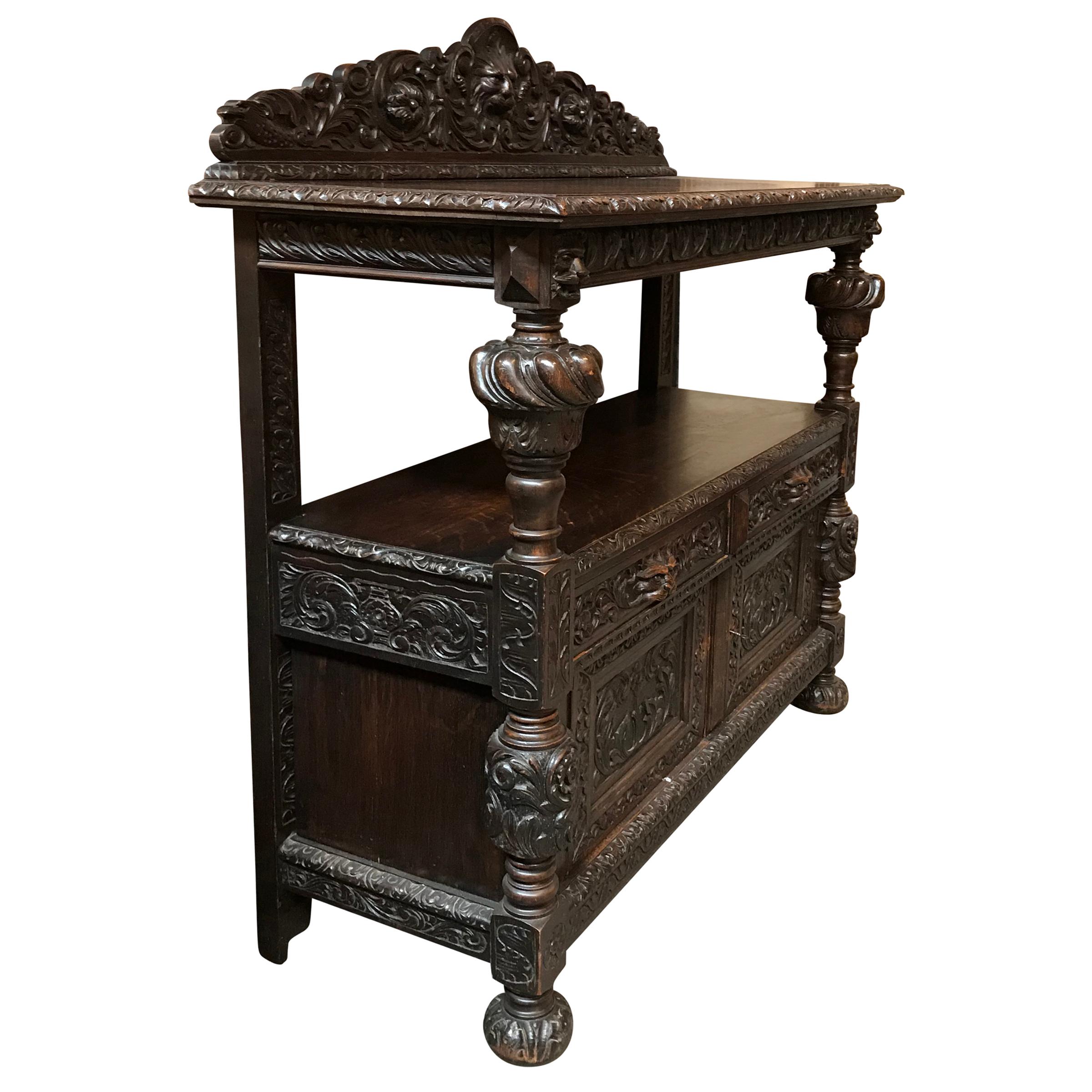 A late 19th century English carved oak sideboard/server by Hewetson, Milner, & Thexton, Ltd., a prominent furniture maker in late 19th century London. The console features highly carved details including the crest-rail at the top with a cat-like