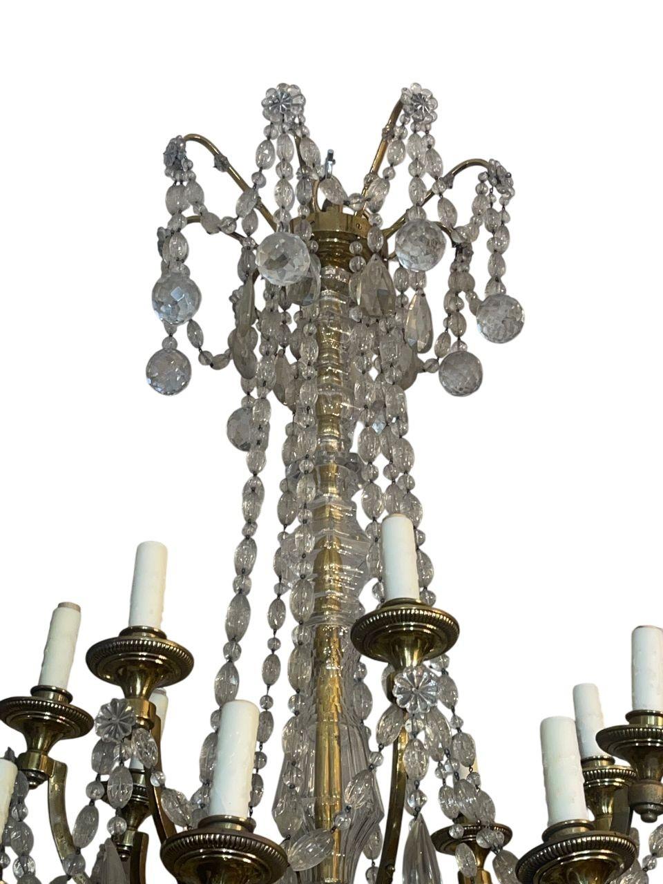 Un grande lampadario inglese di forma classica, realizzato con una struttura in bronzo dorato finemente fusa e riccamente ornata da gocce di cristallo tagliato, rosette e festoni di perline. Il lampadario presenta due livelli di bracci a spirale,