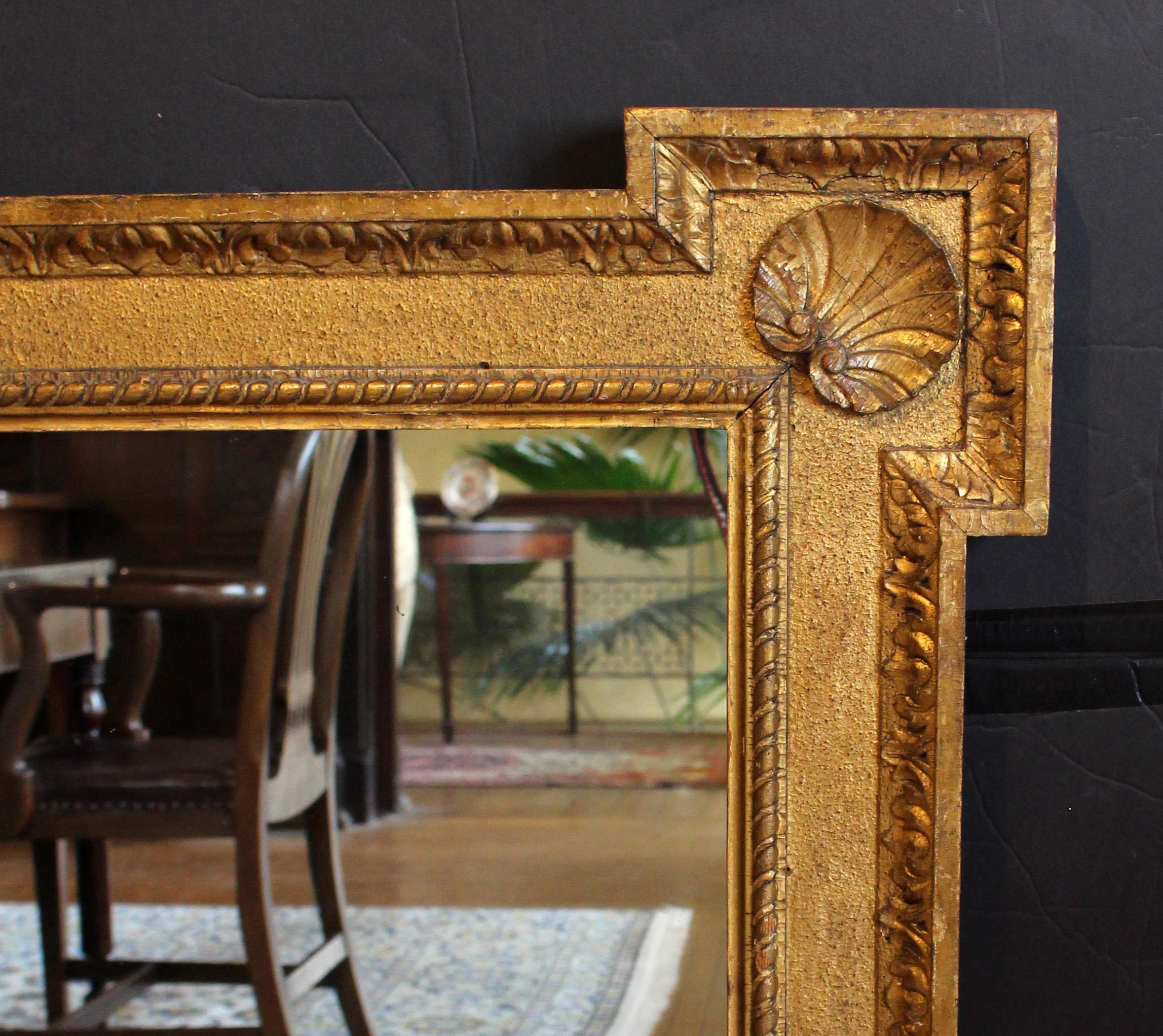 Late 19th century gilt mirror, English. Gilt on wood & gesso; scallop shells on the outset corners, repetitive neoclassical motif inner ribbon border & outer acanthus leaf border. Back framing added and modern mirror plate, most likely originally a