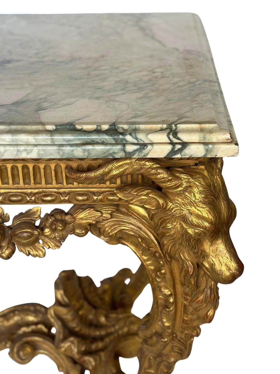 Exceptional Neoclassical giltwood console table, made in England in the Late 19th Century, consisting of a hand-carved giltwood table frame having ram heads and feet, as well as a center figure of a putti with a fish-looking tale. The console is