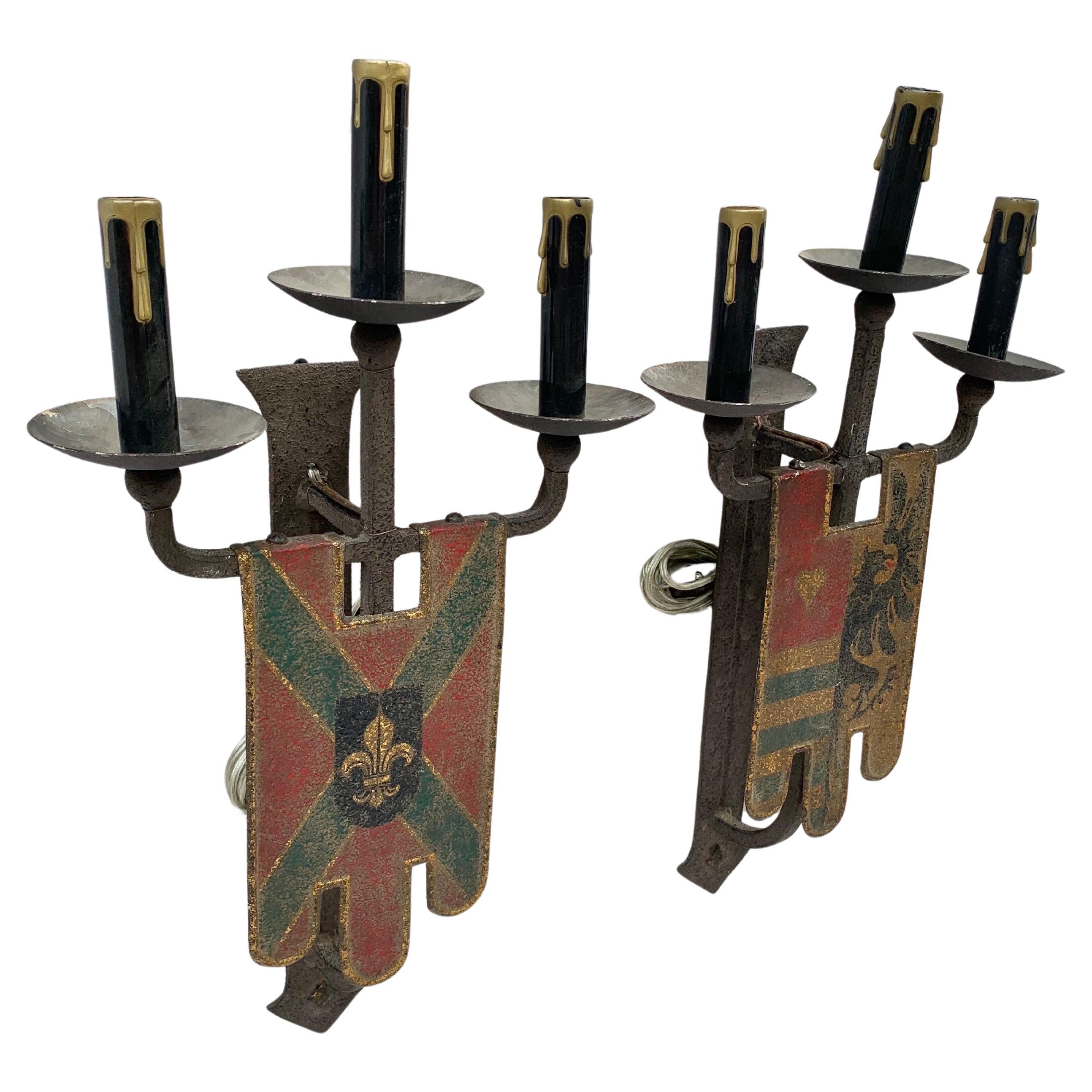 Questa coppia di applique della fine del XIX secolo è stata realizzata in Inghilterra nel 1800. Ogni applique in ferro forgiato a mano ha la forma di uno scudo e raffigura uno stemma intricato dipinto a mano. Le appliques hanno tre luci a candelabro