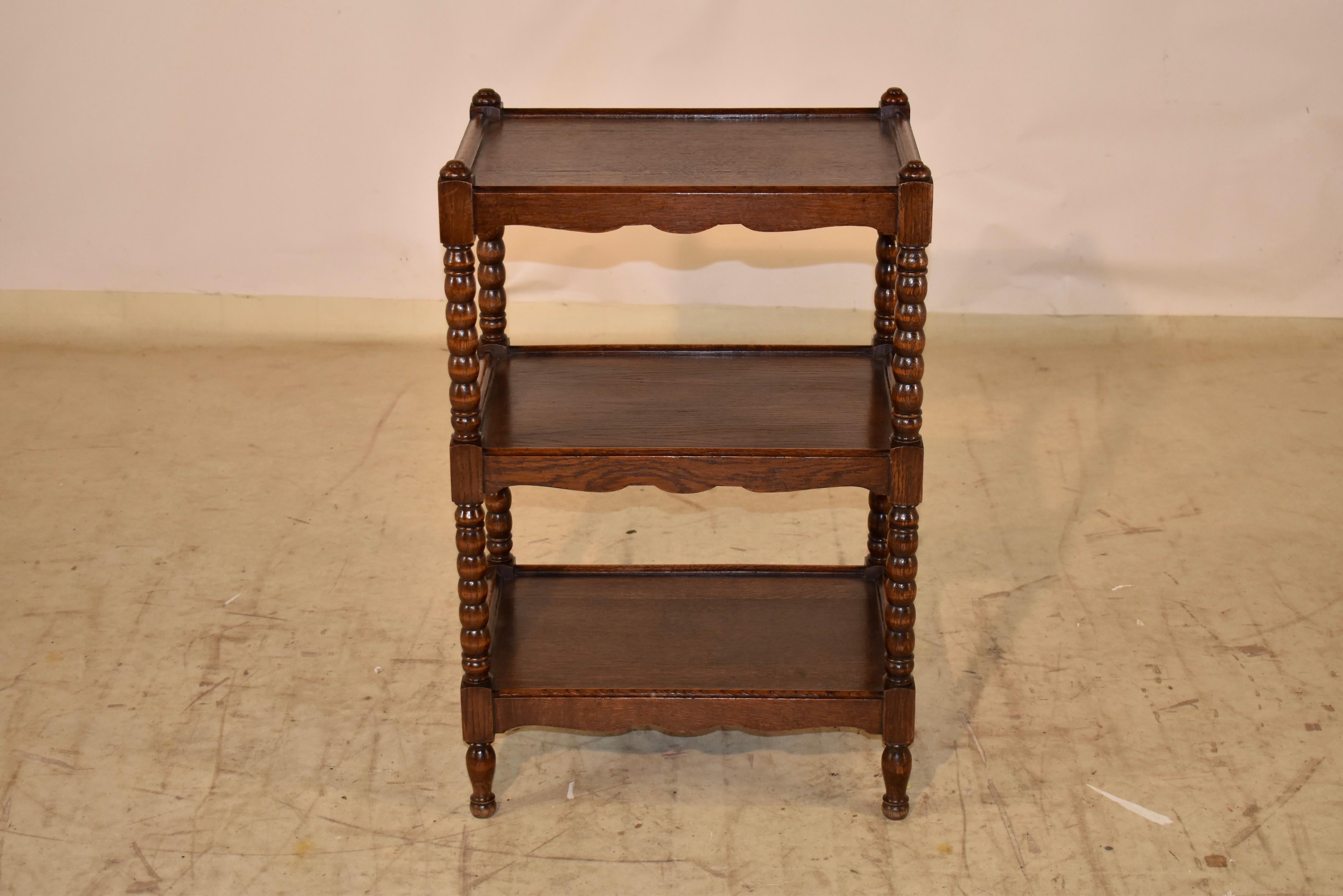 19th century oak drinks cart from England.  The top of the legs are decorated on top with hand turned caps, over three shelves, all joined by hand turned spool legs.  The shelves have hand scalloped aprons and  slightly raised and routed edges.  The