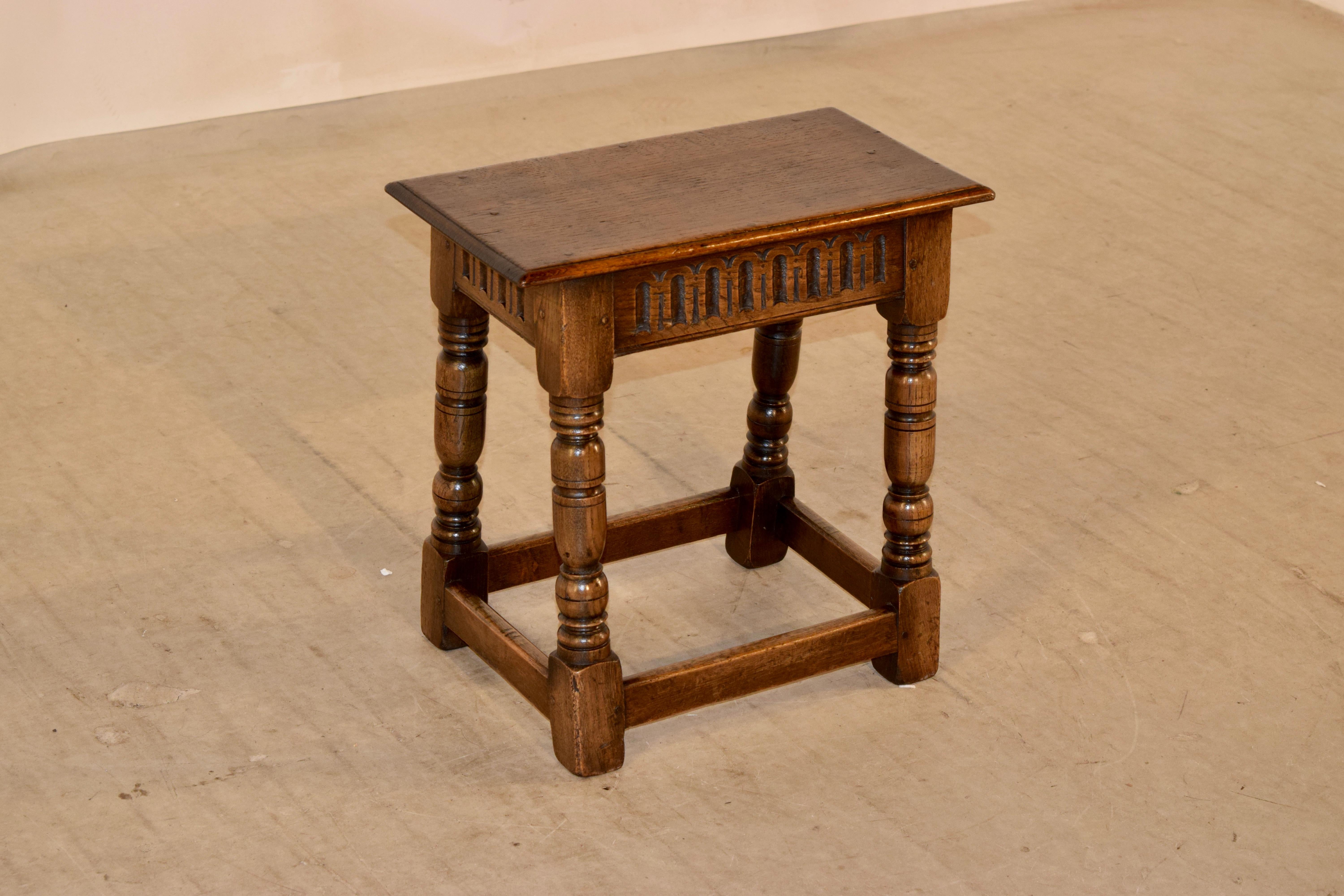 Late 19th century oak joint stool from England. It has a beveled edge around the seat, following down to a hand-carved fluted apron and raised on splayed, hand-turned legs, joined by simple stretchers.