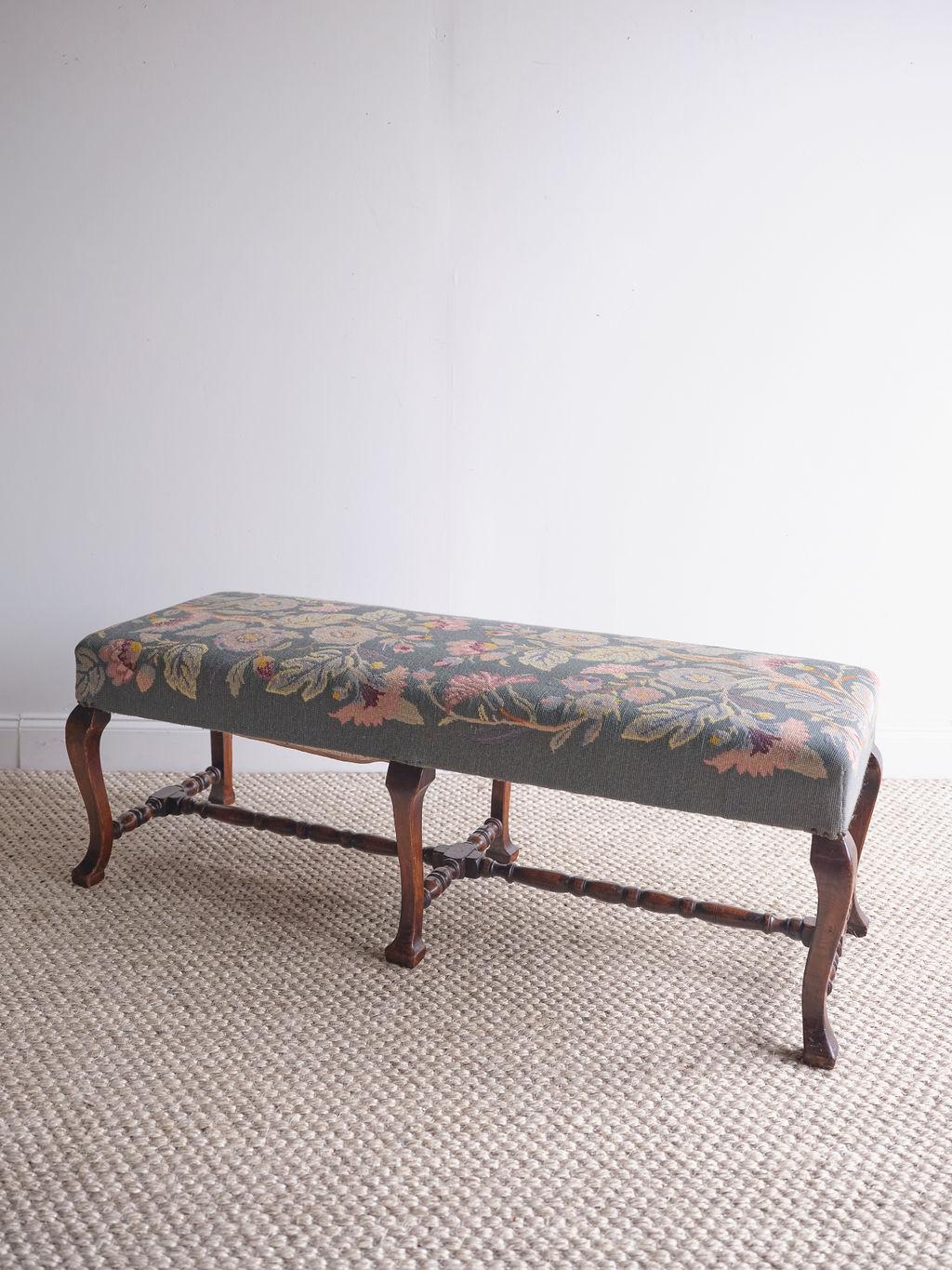 This lovely hand stitched needlepoint stool features elegant light pink, dark pink, and yellow flowers with a light blue background. The ottoman rests on 6 ornate dark stained oak legs with a base connecting the legs. Because the seat of this piece