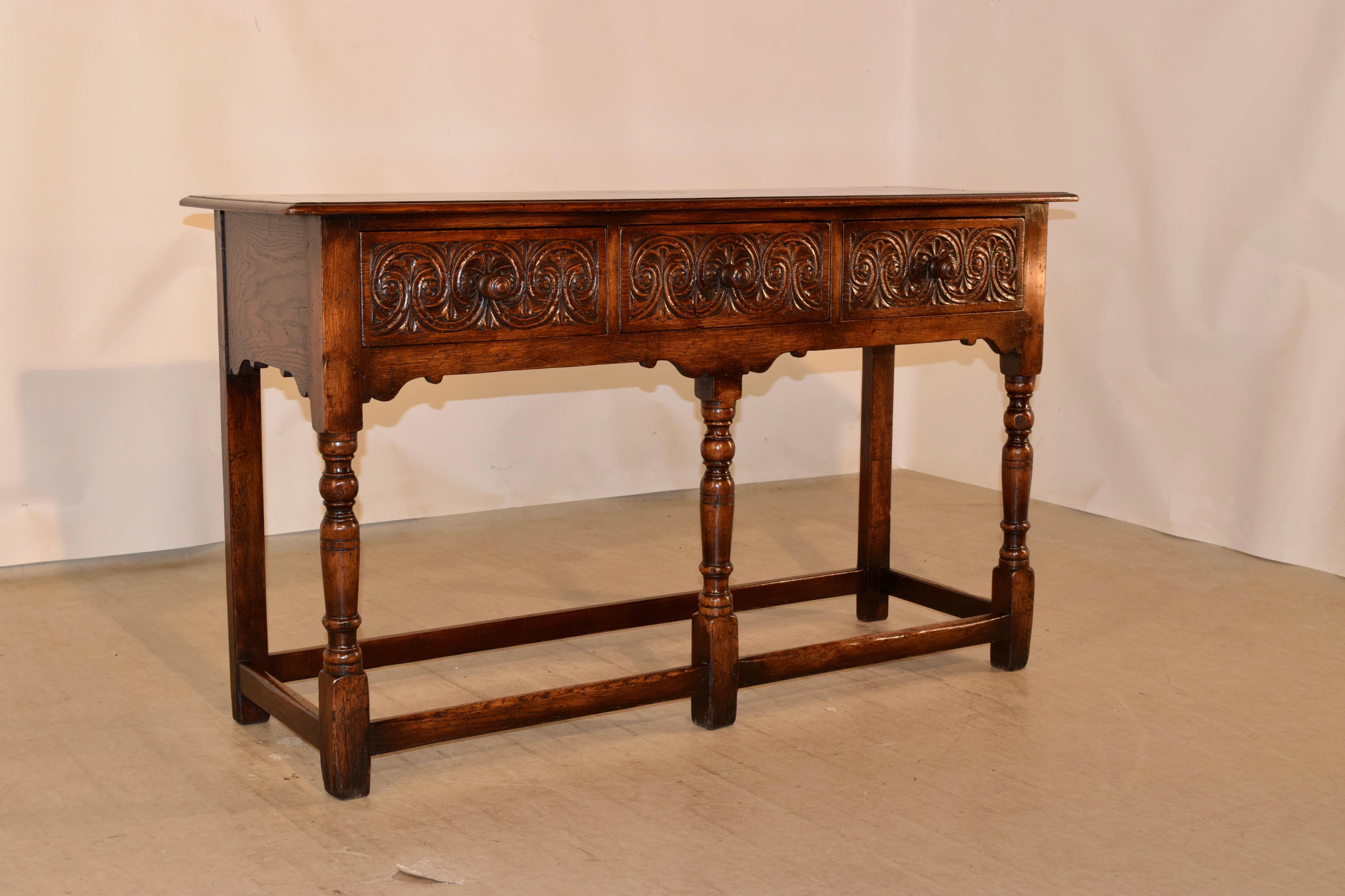 Late 19th century oak sideboard from England with a beveled edge around the top, following down to simple sides which are serpentined and three drawers in the front, all with hand carved drawer fronts. The legs are hand turned in the front and