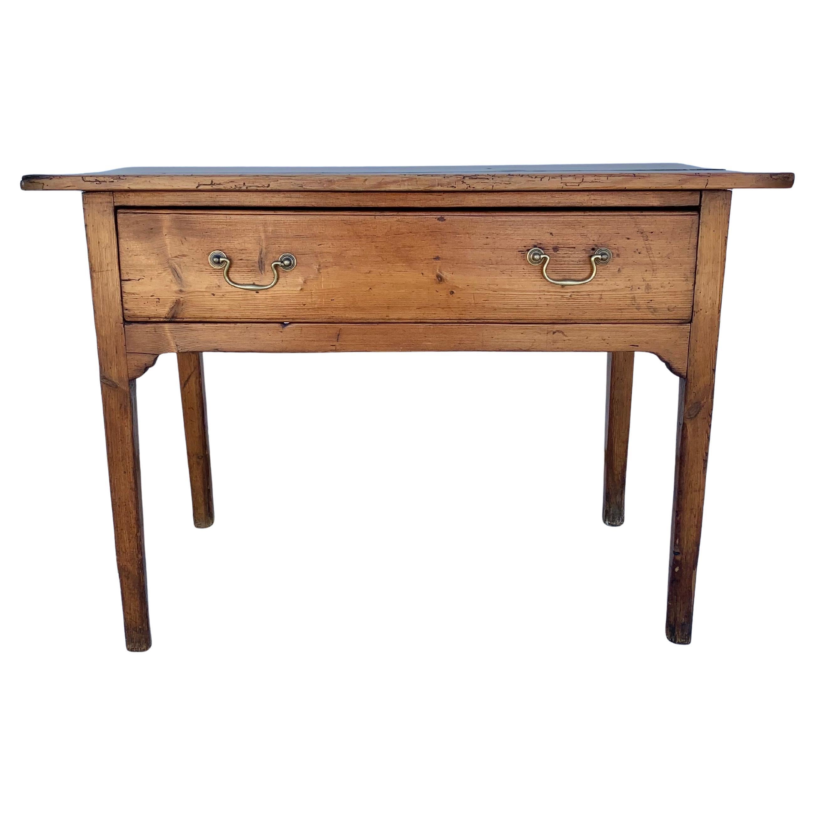 Trouvée en Angleterre, cette table de la fin du XIXe siècle a été fabriquée en pin ancien à la fin des années 1800. La table présente un plateau à deux planches reposant sur un grand tiroir simple. Le tiroir à queue d'aronde est orné de poignées en