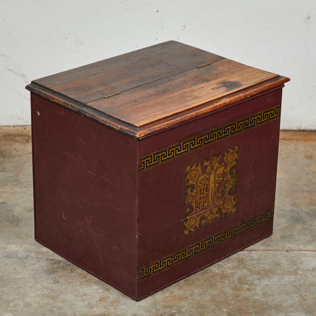 Late 19th-century English imported storage box with hand-painted  gilt Chinese character insignia and Greek key pattern. Features a jointed, hand-carved wooden top and tin siding in a rich maroon color. 

England, circa 1880

Dimensions: 22.5W x 17D