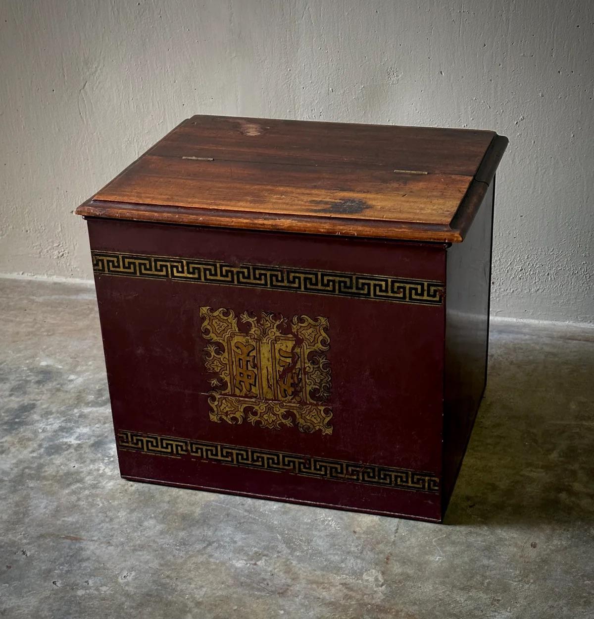 This late storage box blends Eastern and Western aesthetics with its hand-painted gilt Chinese character insignia and a Greek key pattern that encircles the rich maroon tin siding. The box is topped with a jointed, hand-carved wooden lid, adding a