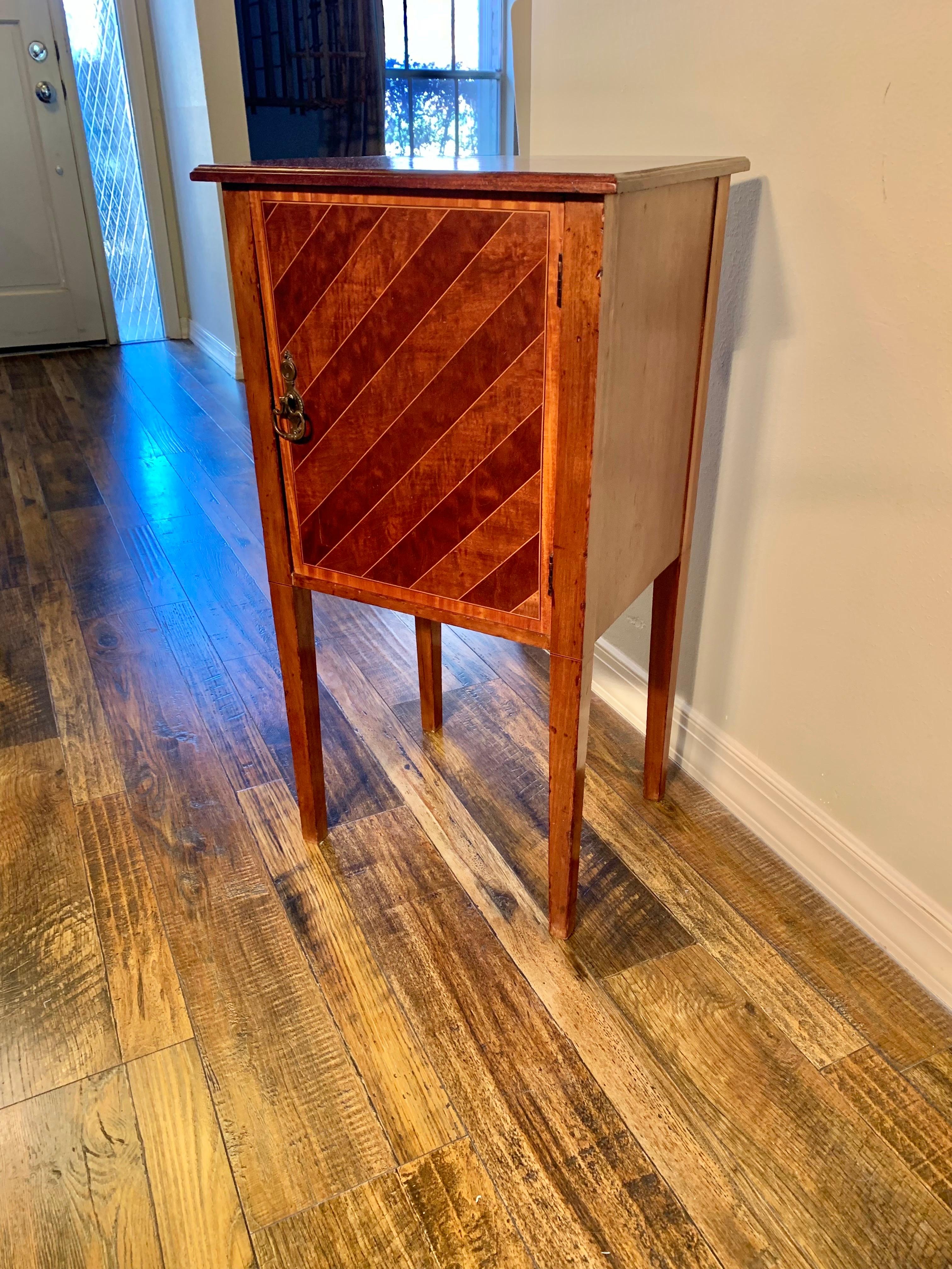 Found in England, this Cabinet or Side Table was crafted by English artisans from old growth walnut in the 1890's. The piece features an inlay wood banded top resting above an inlay wood door that opens to reveal two shelves for storage. The cabinet