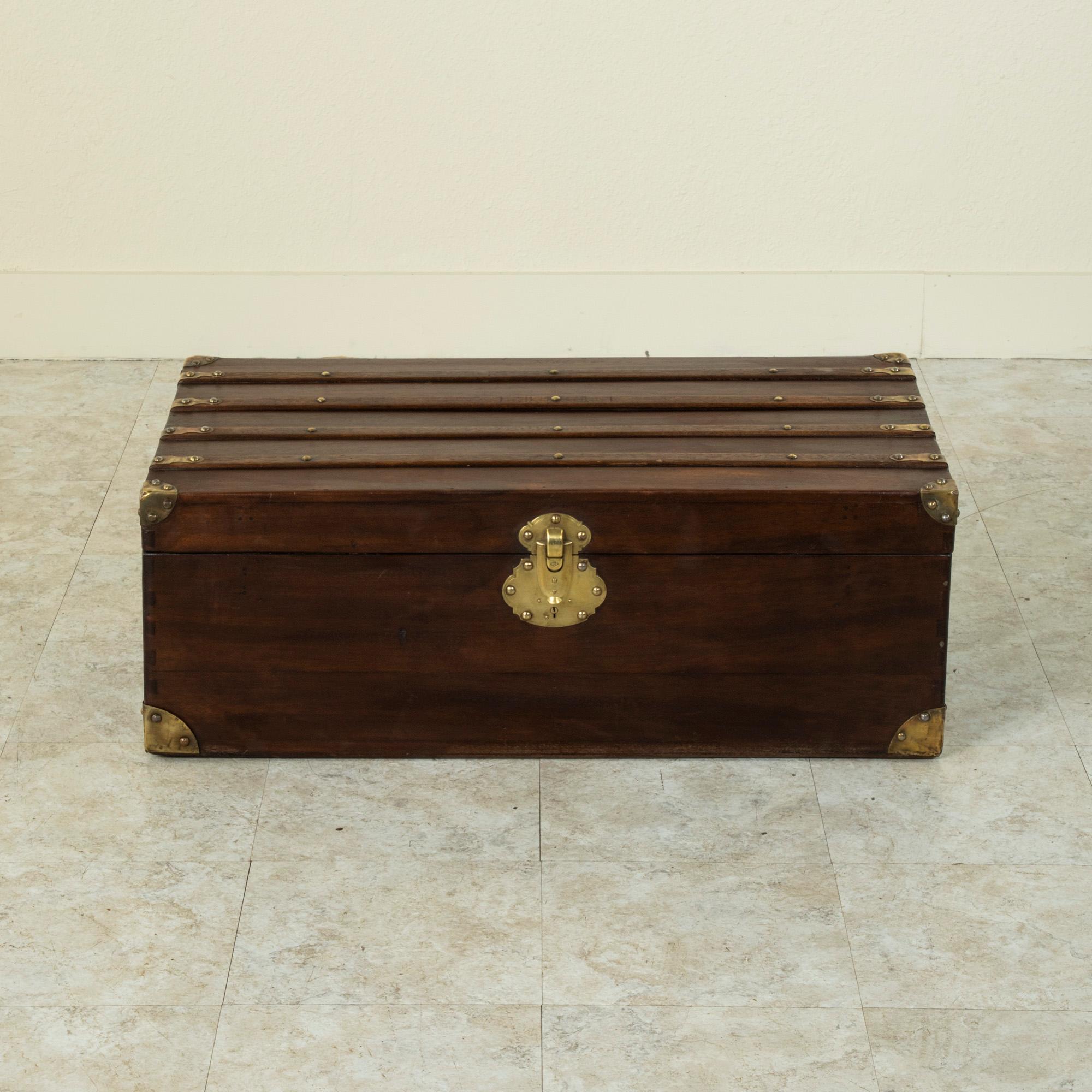 This French walnut steam trunk from the turn of the 20th century features wooden runners detailed with brass rivets and its original brass locks. Its corners are also capped in brass which offered protection from damage when traveling. The brass