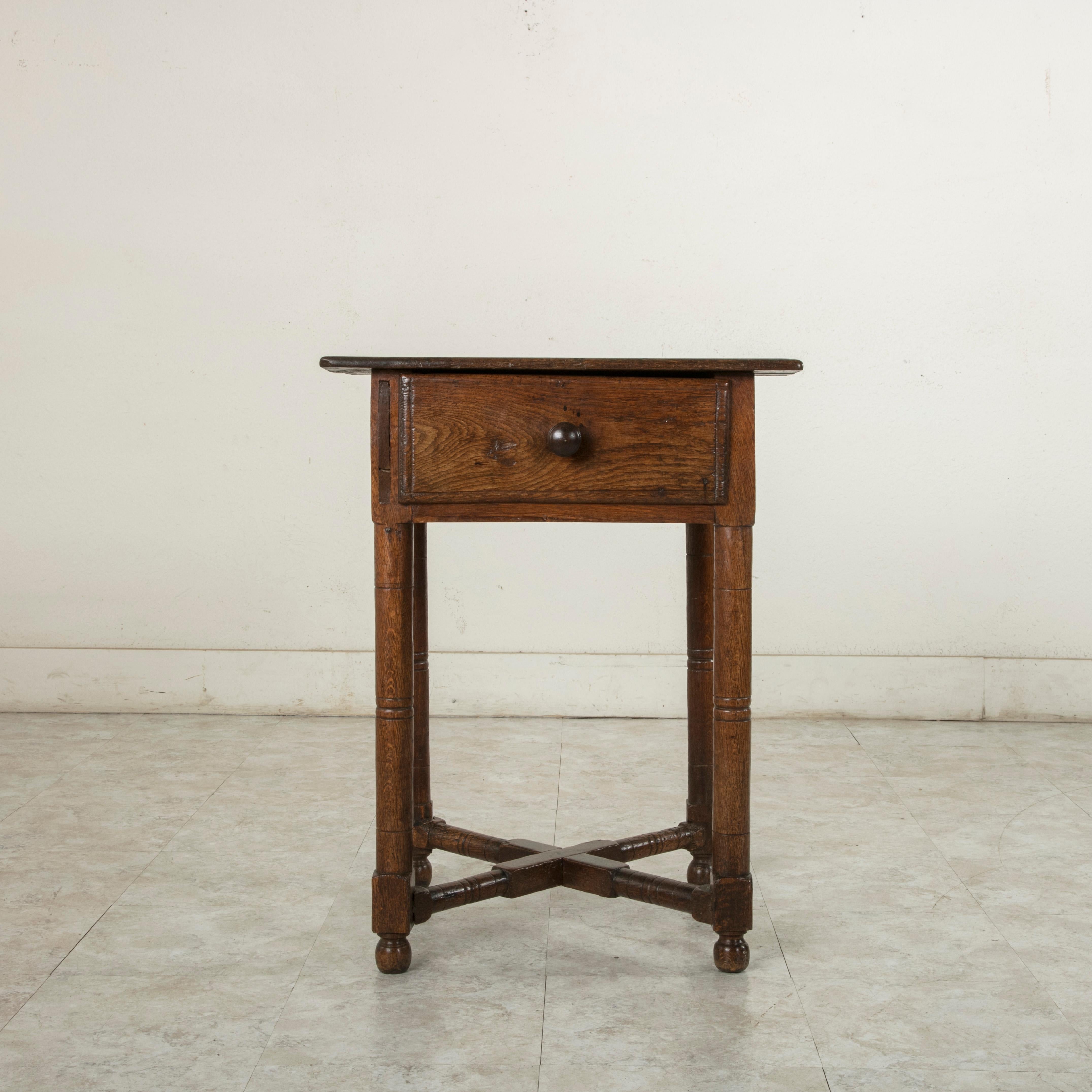 This late 19th century French artisan made oak side table features hand pegged mortise and Tenon joinery and a beveled top.
Its single drawer is fitted with a knob drawer pull, and its turned legs are joined by an X-stretcher to provide stability,