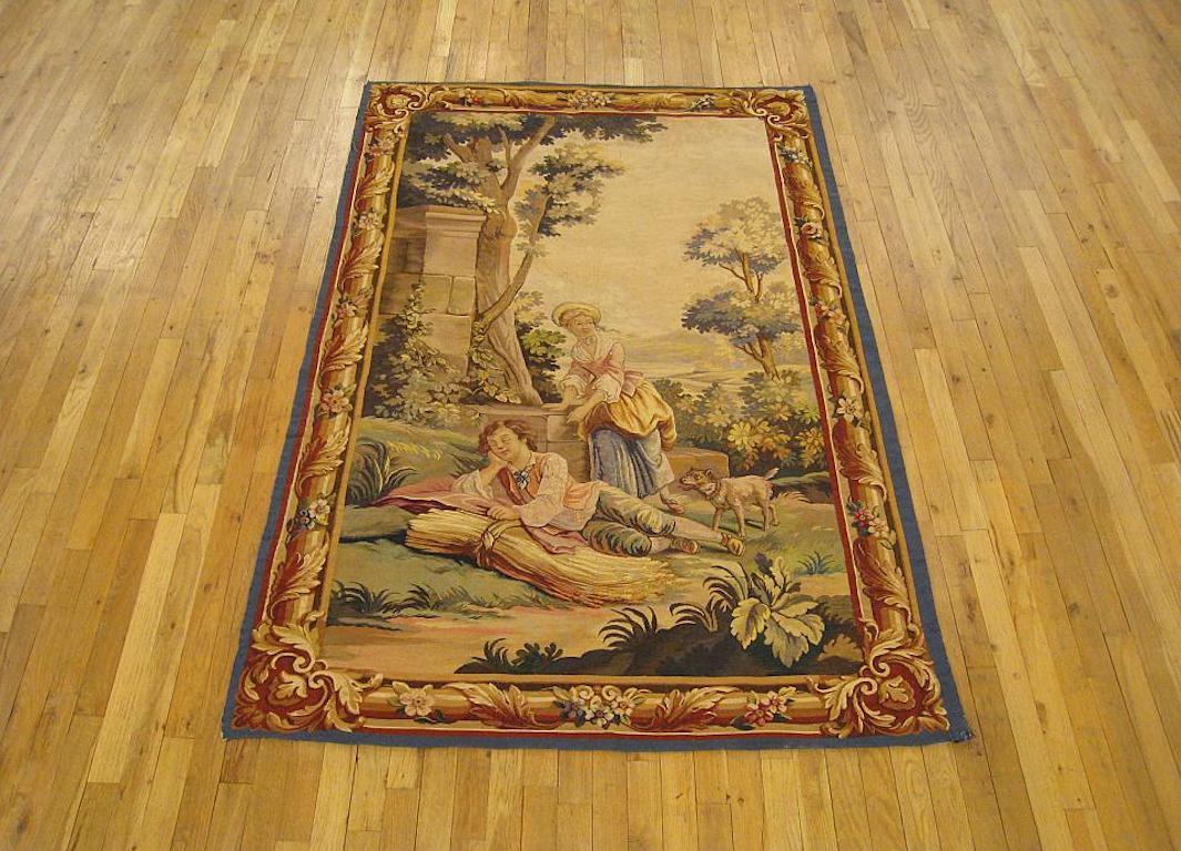 A French Aubusson tapestry from the late 19th century, featuring a rustic scene with a young man reposing on a bundle of hay while his damsel and her dog look on. Enclosed with a trompe l’oeil picture frame border. Wool with silk inlay. Measures: