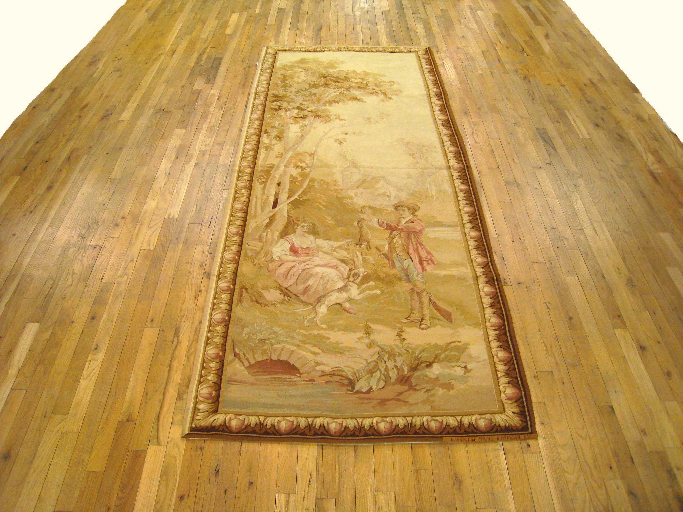 Panneau de tapisserie rustique d'Aubusson datant de la fin du XIXe siècle, représentant une scène dans laquelle un jeune homme présente à son chien avide le gibier qu'il a attrapé à la chasse, tandis que sa fiancée, assise sous un arbre à gauche, le