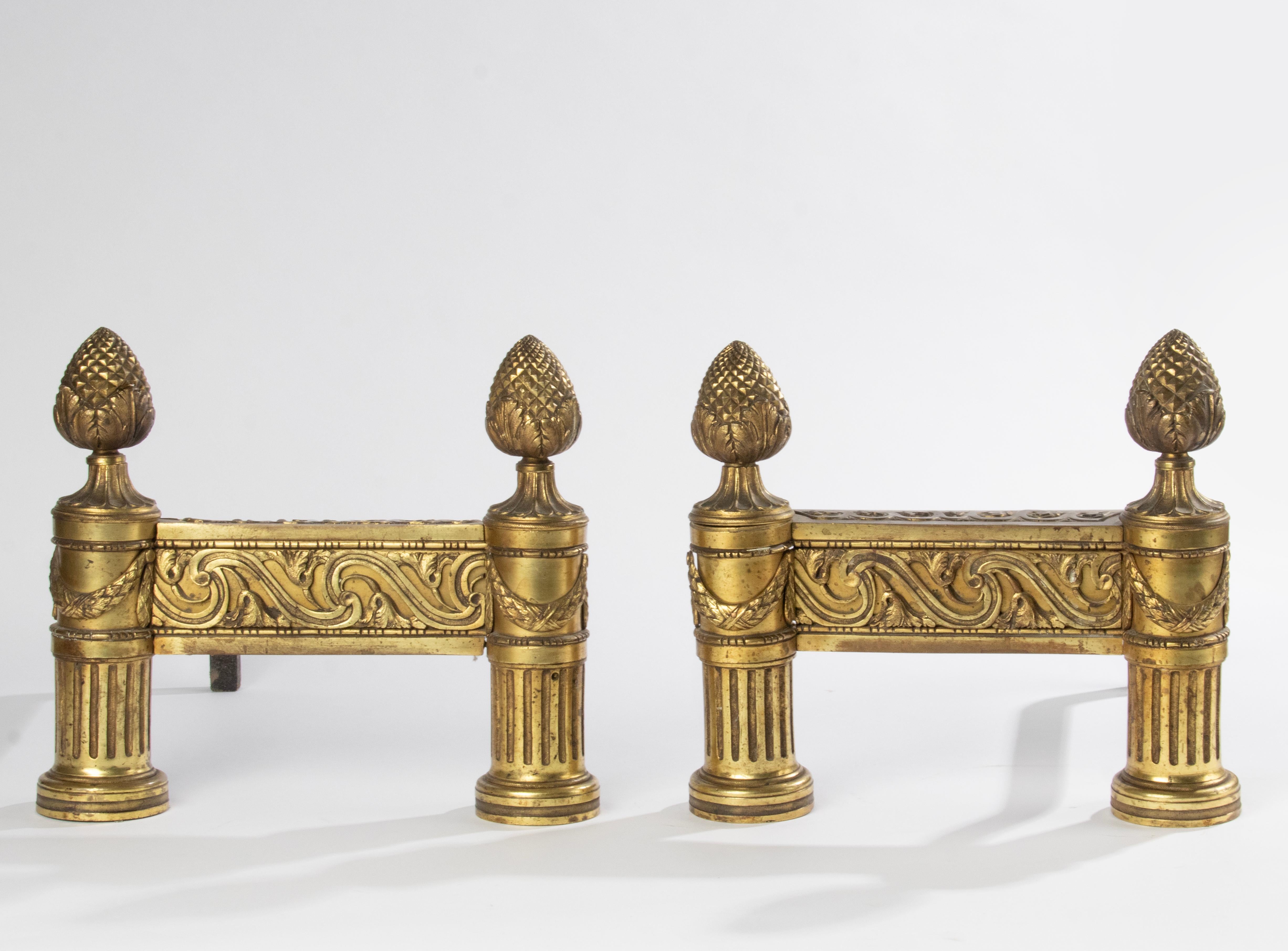 A pair of late 19th century French andirons, in France called ‘Chenets’. Richley decorated with scrolls on the front fries. Standing on fluting columns with a flower garland and with pine cone endings. The back rests are made of forged iron, these