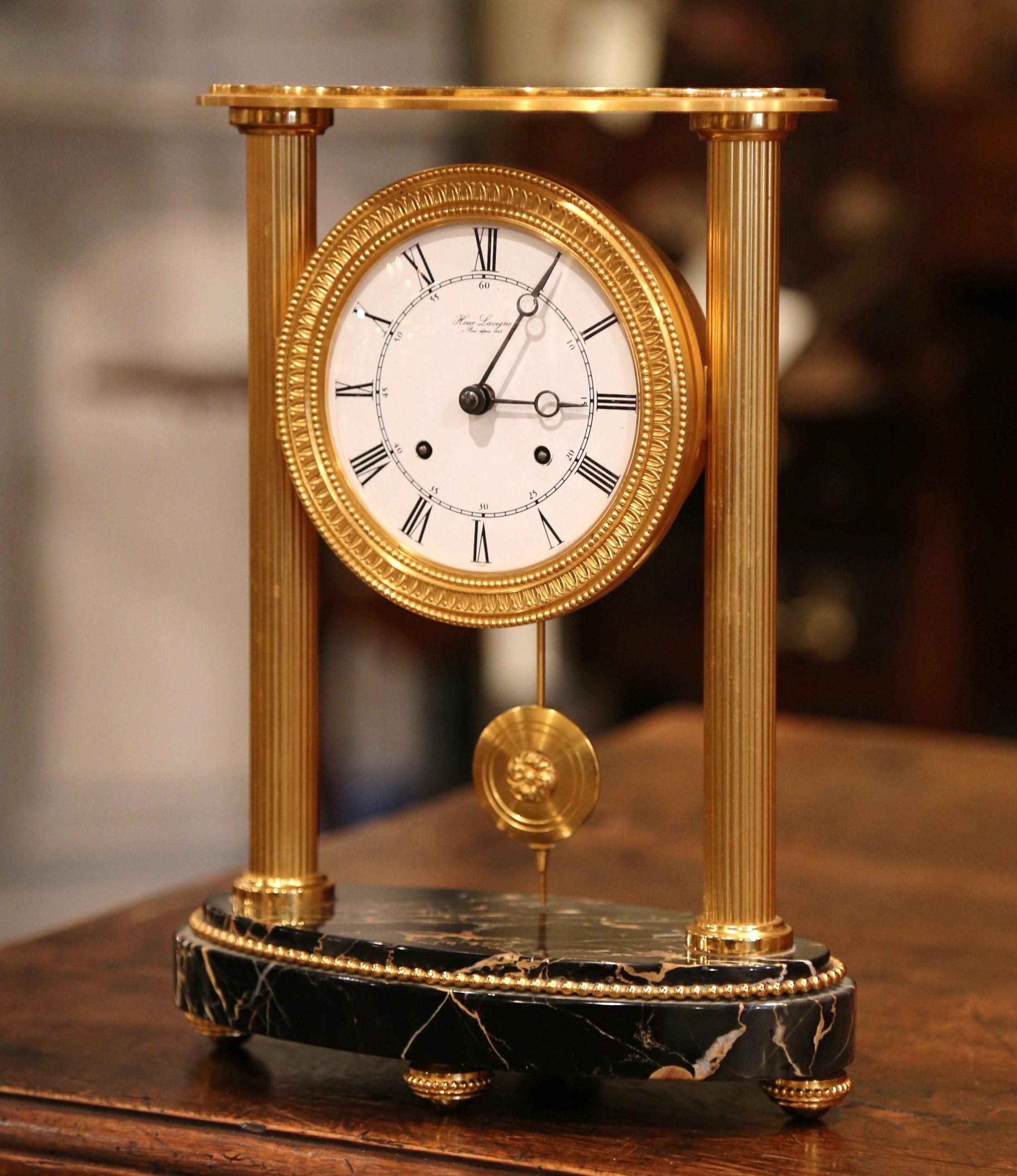 This elegant antique table clock was created in Paris, circa 1890. Oval in shape, the clock sits on a black marble base over four small round feet. The desk clock features bronze columns on each side, which hold a porcelain clock face signed Hour