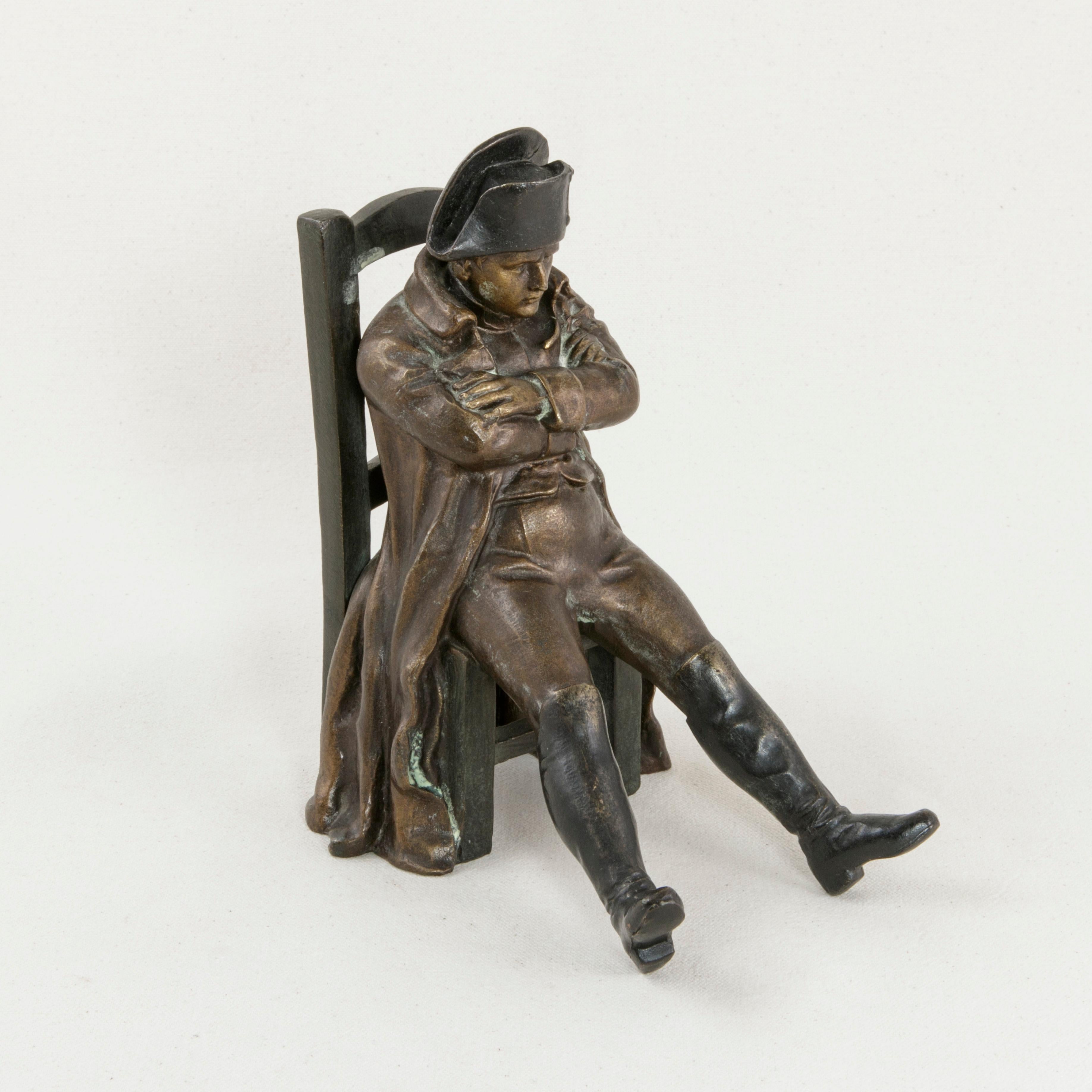 This late 19th century French bronze sculpture depicts Emperor Napoleon Bonaparte seated in a ladderback chair with legs outstretched and arms folded across his chest in a relaxed pose. An unusual piece with a warm patina depicting Napoleon at ease,