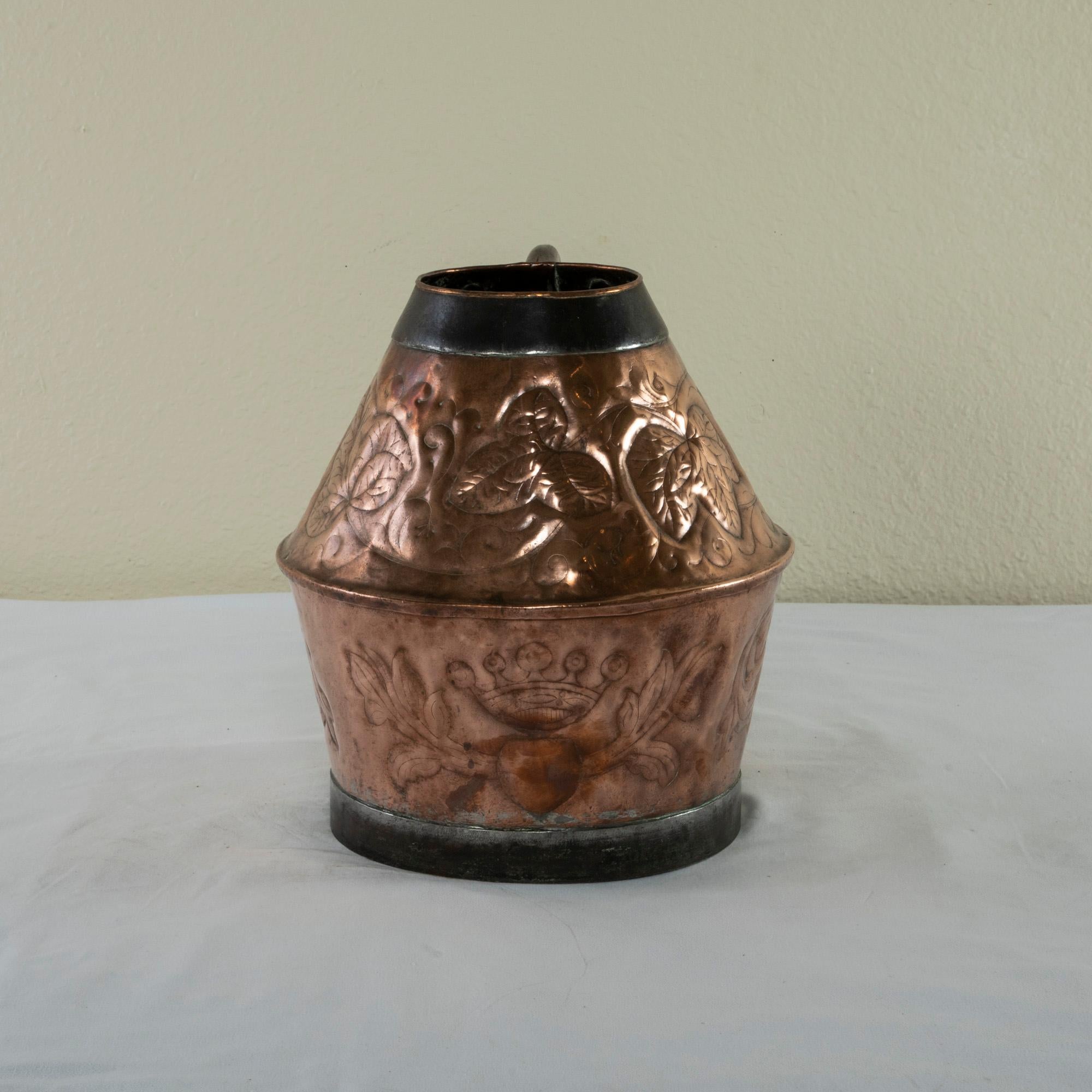 Originally used in a chateau, this large scale late 19th century French copper repousse pitcher features three shields on it lower half, each flanked by scrolling leaves. One of the shields depicts a rooster and another has a crown above it. The